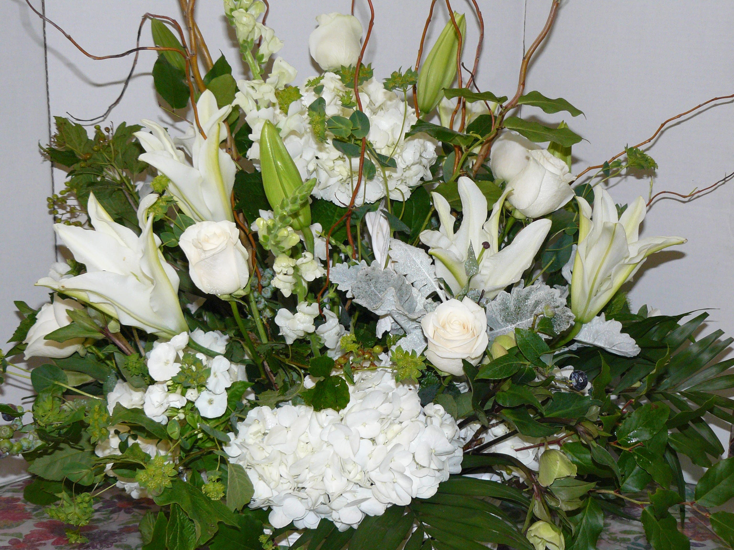 Large white floral arrangement with lilies, roses, and hydrangeas