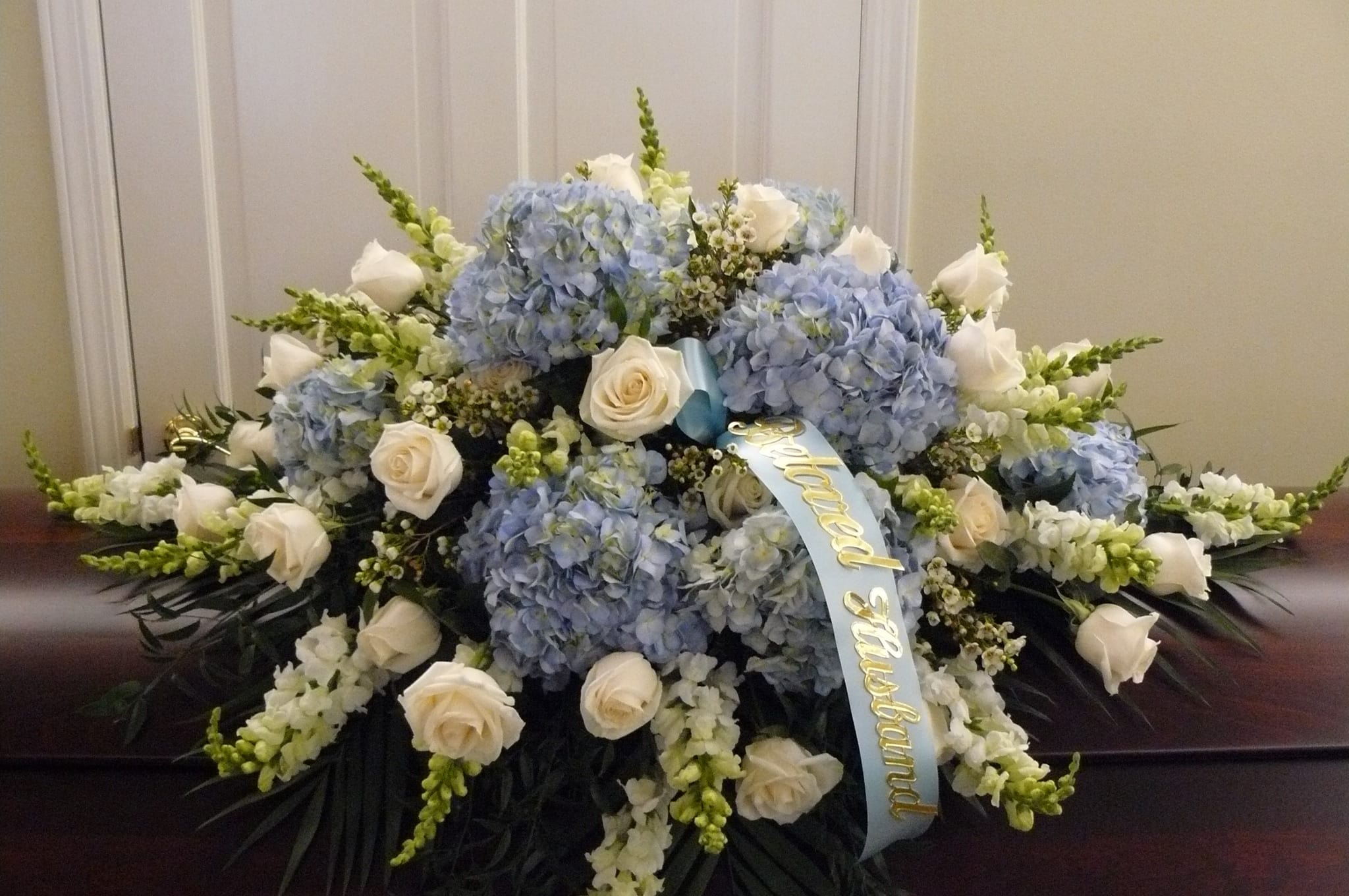Blue &amp; White Casket  Cover   (Click on Picture for Best View) -  Casket Spray is a wonderful way to commemorate a life abundant in beauty and love. Blue Hydrangea, White Roses, White Snap Dragons, Wax Flower Palms are elegantly arranged among an assortment of lush greens to create a sophisticated display meant to bedeck the top of their casket at the final memorial service. Your purchase includes a complimentary personalized gift message.