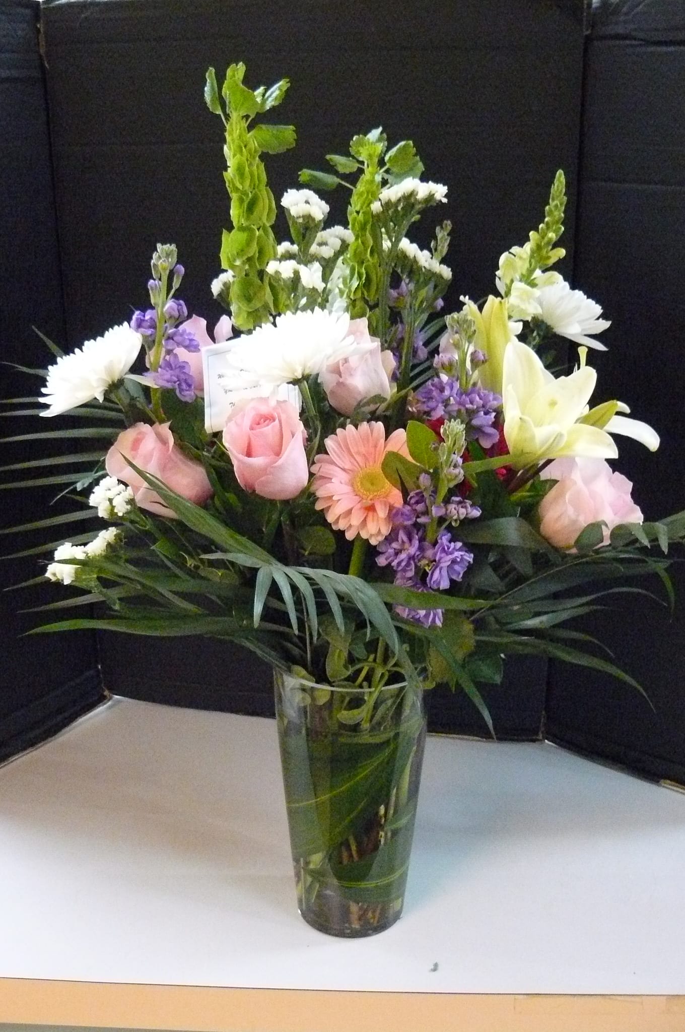Mixed bouquet of pink roses, white lilies, and purple flowers in a glass vase