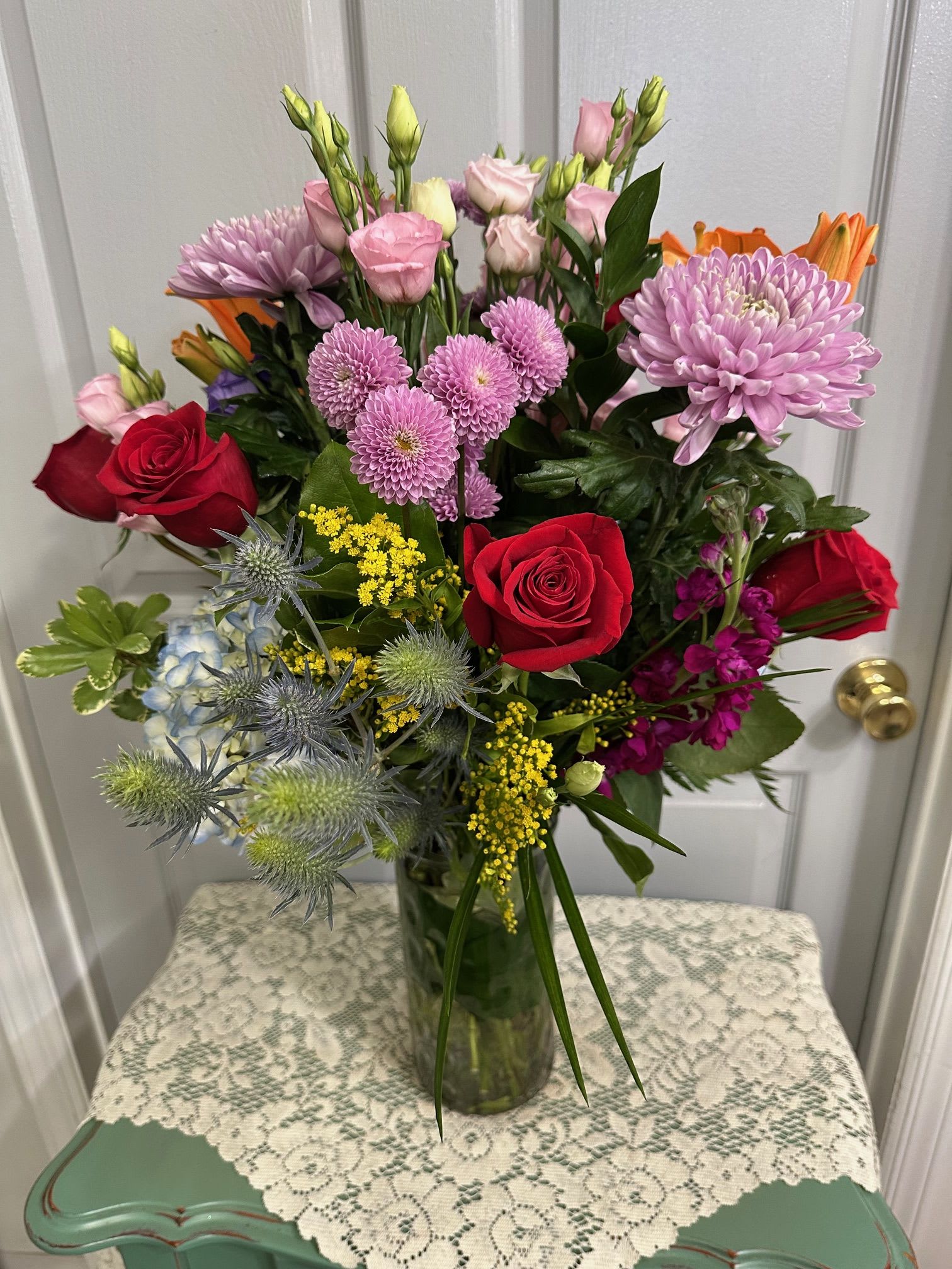 Mixed bouquet of red roses, pink blooms, and lavender flowers in a glass vase