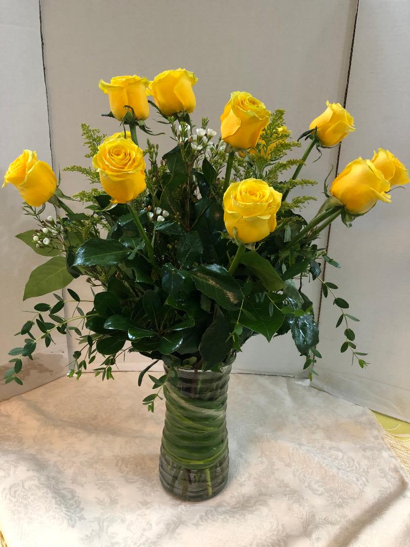 Yellow roses arranged in a clear glass vase with greenery