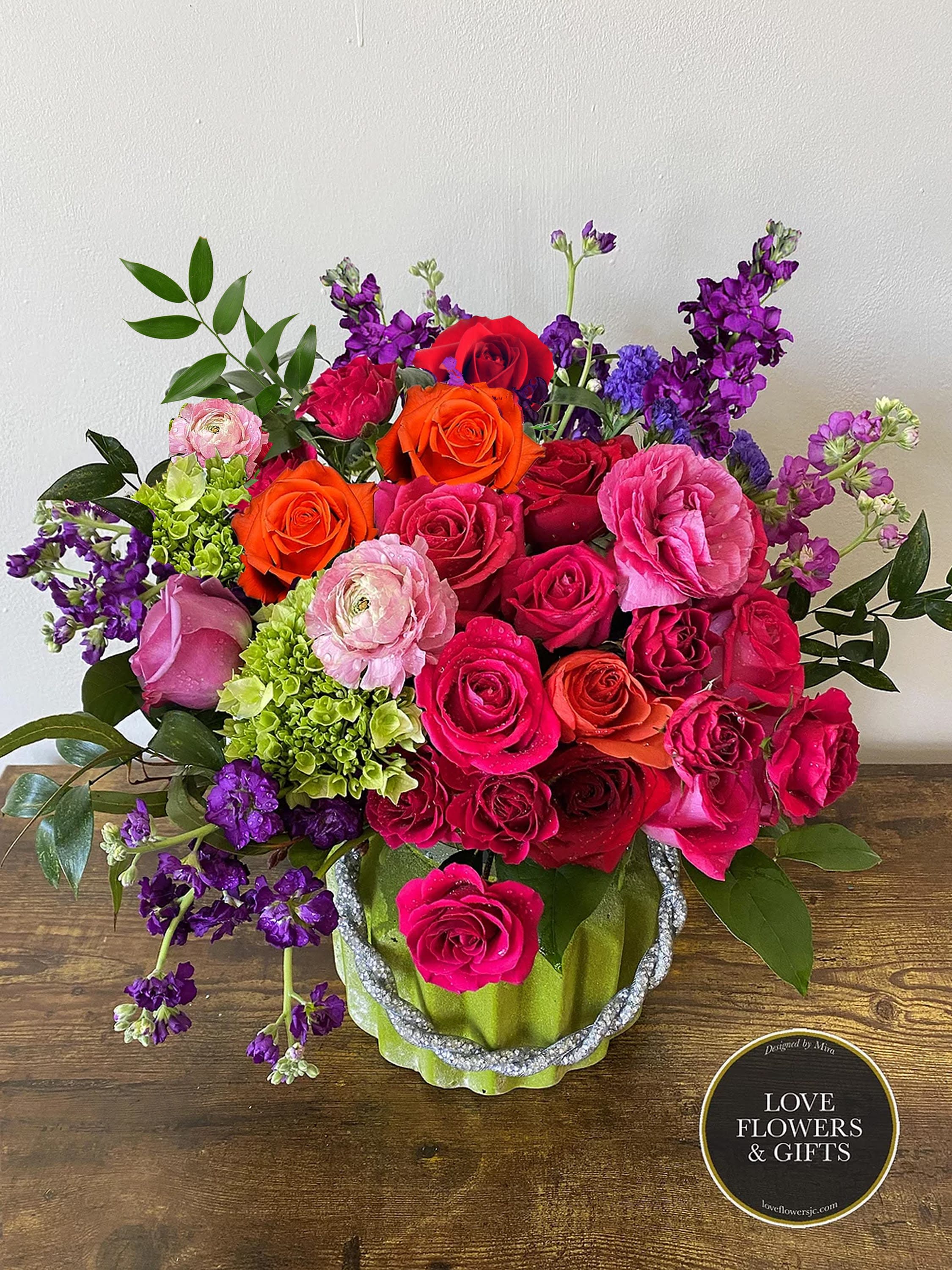 Bright mixed arrangement of pink, red, orange, and purple flowers in a green ceramic vase.