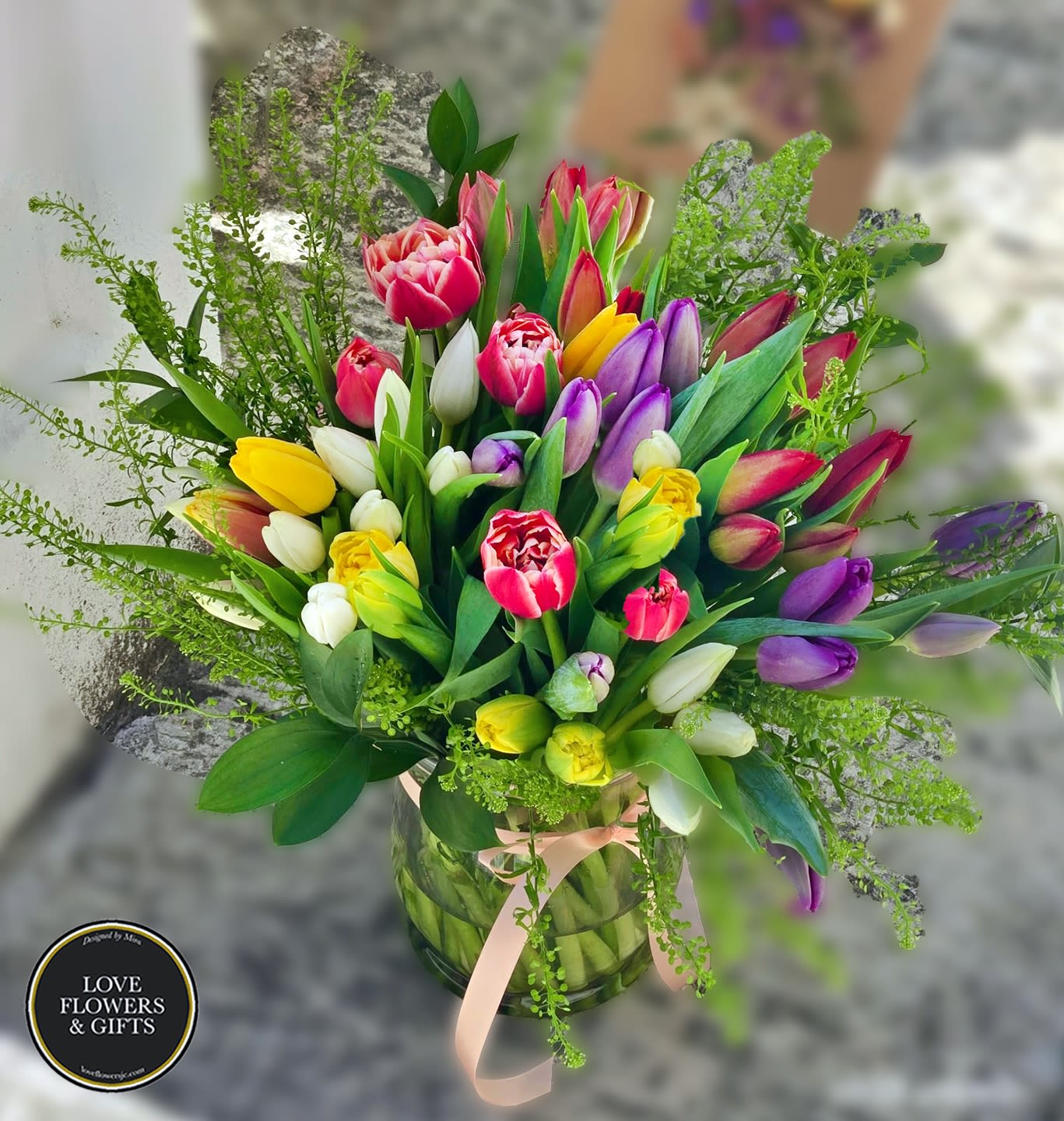 Mixed tulip bouquet in a glass vase with a pink ribbon