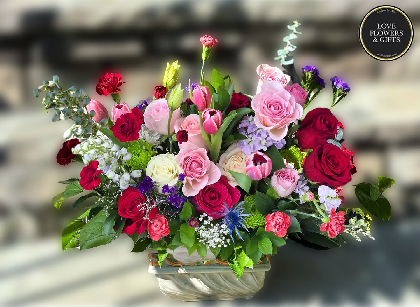 Ruby Fit  - Lush layers of pink and red roses, bright pink tulips, and mini carnations centerpiece arranged in a decorative ceramic vase. 