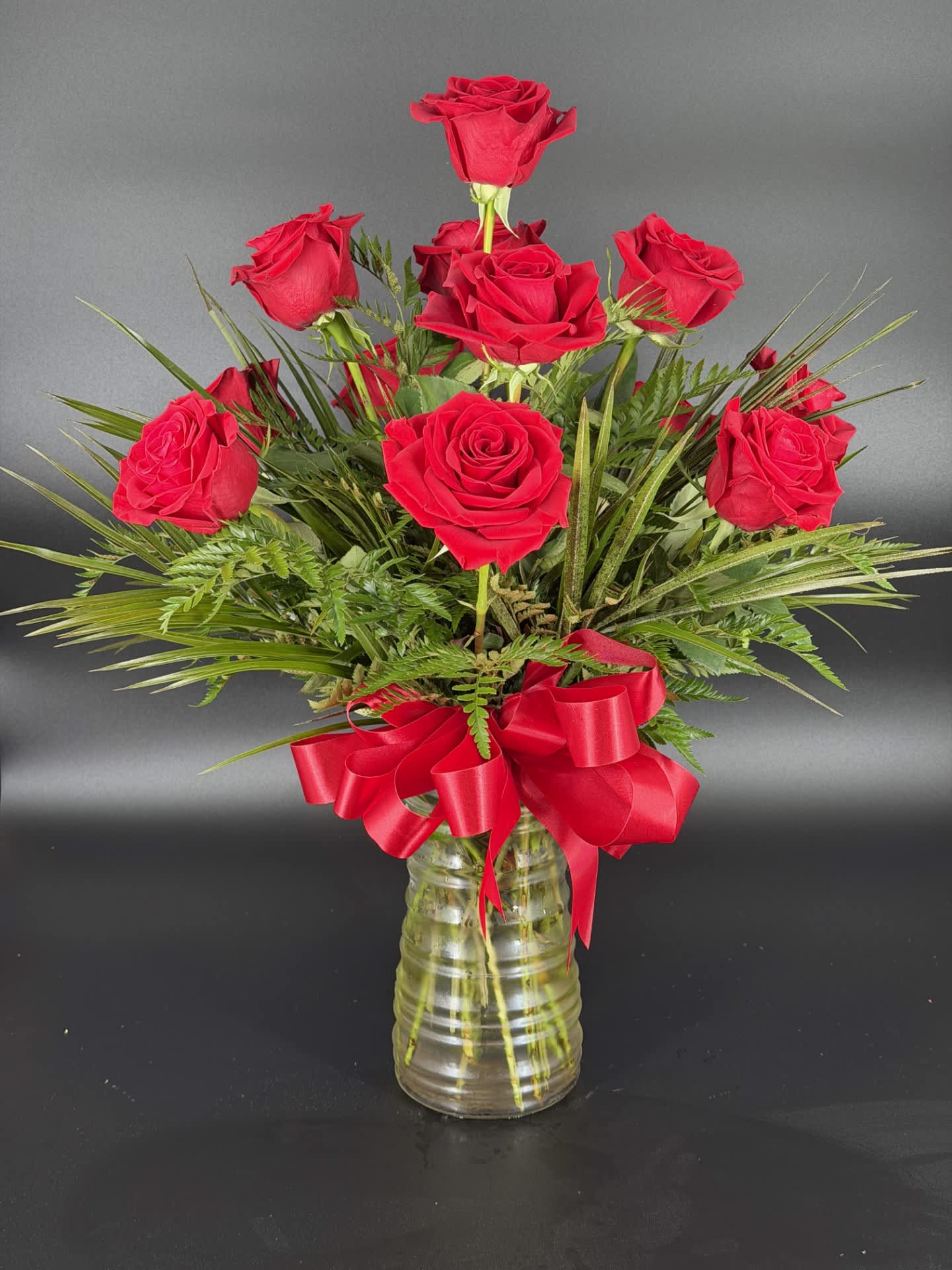 Red roses arranged in a clear glass vase with a red ribbon bow