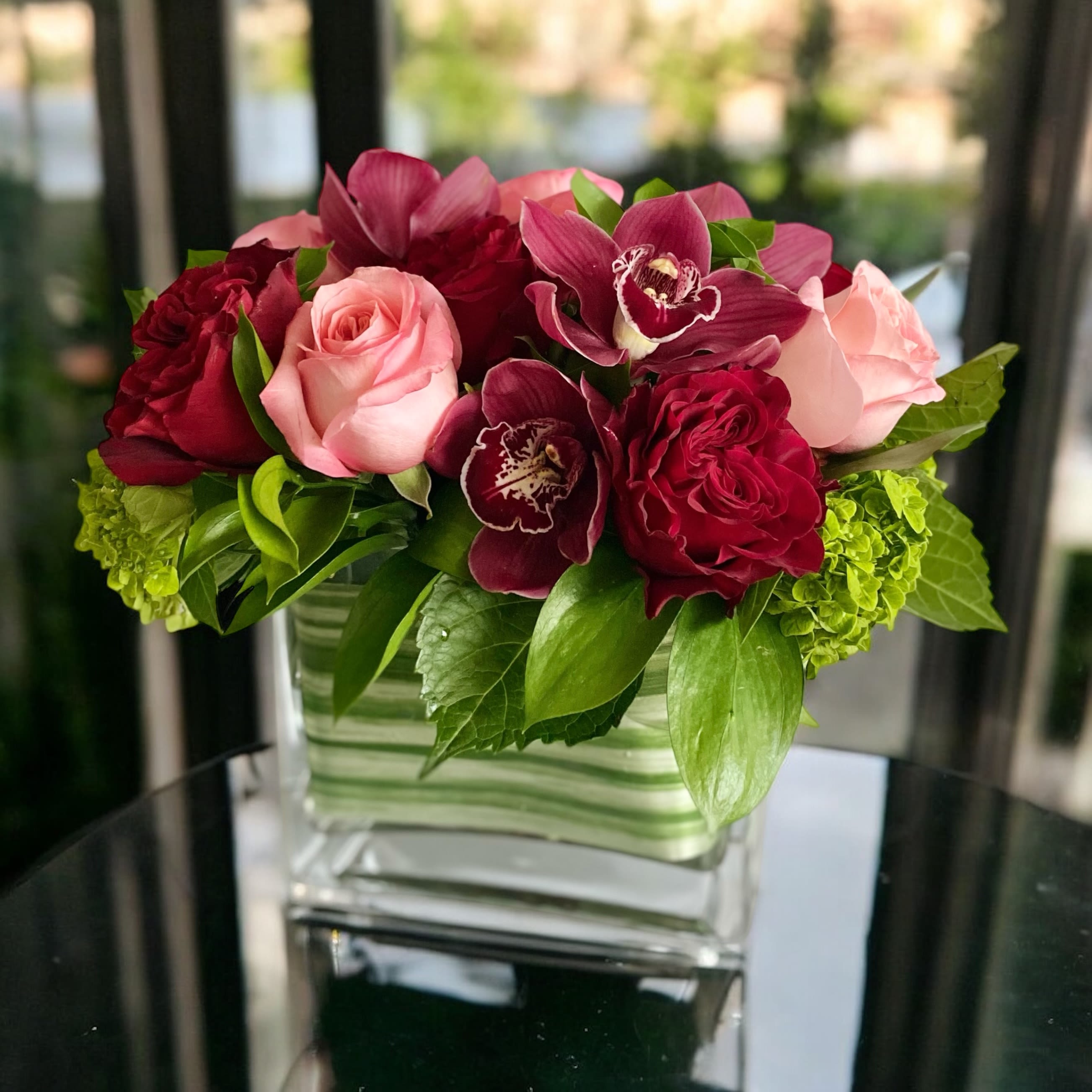 Pink and burgundy roses with orchids in a glass vase