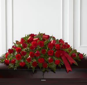 Red rose casket spray with a red ribbon on a dark casket