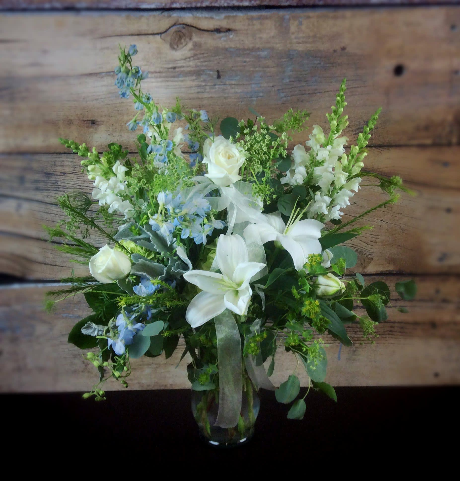 White lilies and roses with blue flowers in a glass vase