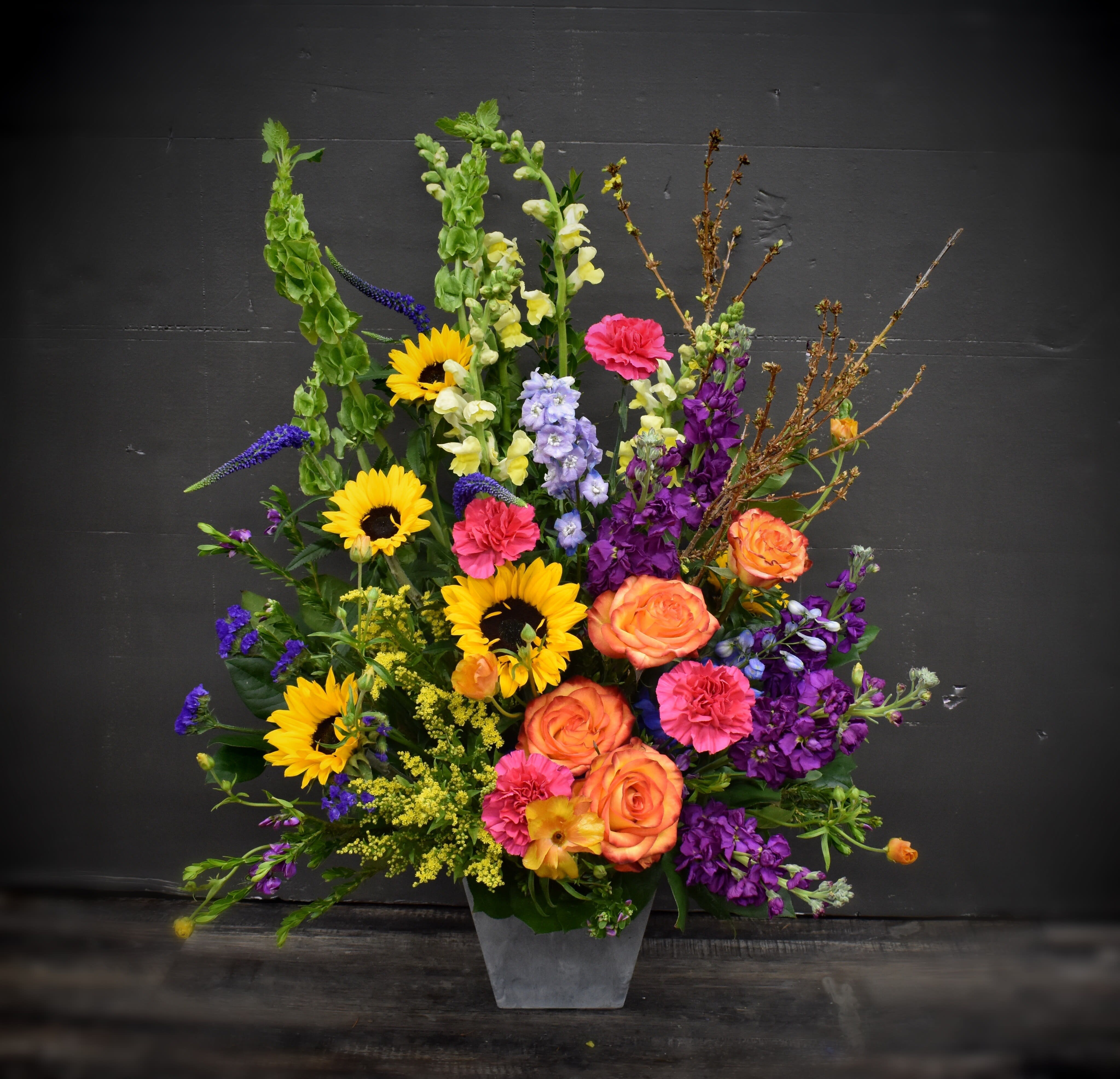 Colorful mixed flower arrangement in a gray vase with sunflowers and roses
