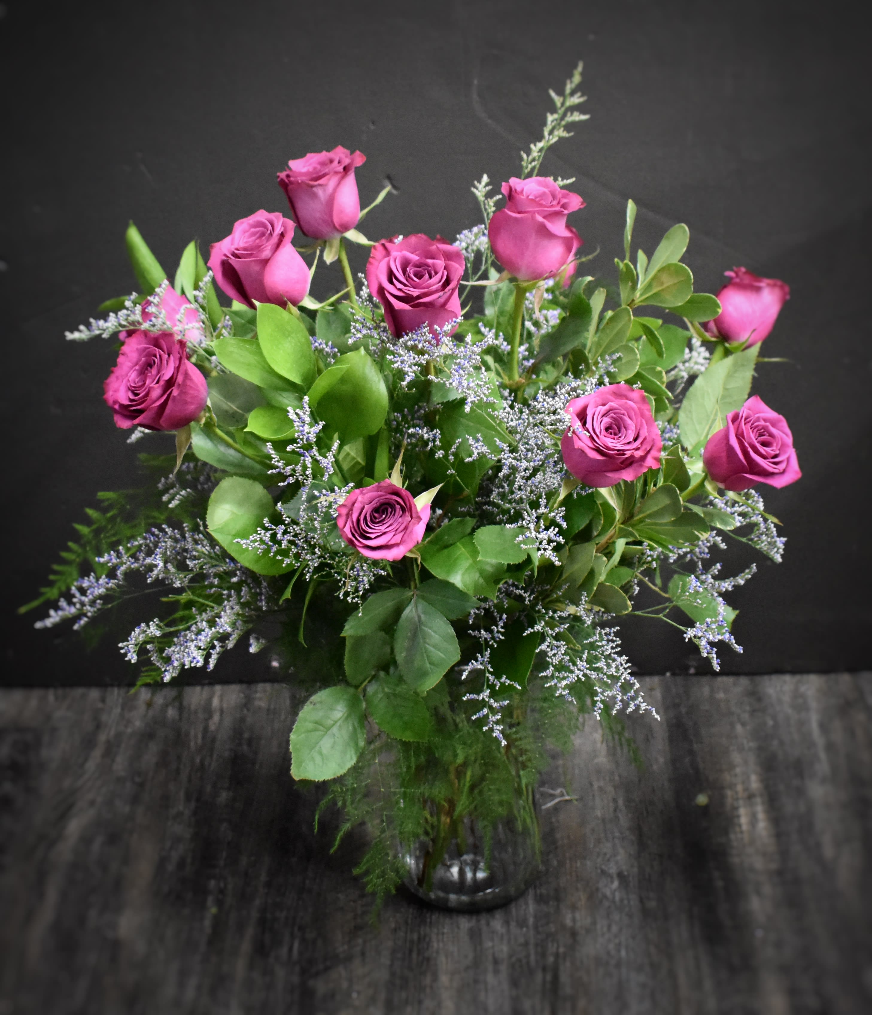 Arrangement of deep pink roses with soft lavender filler flowers in a clear glass vase