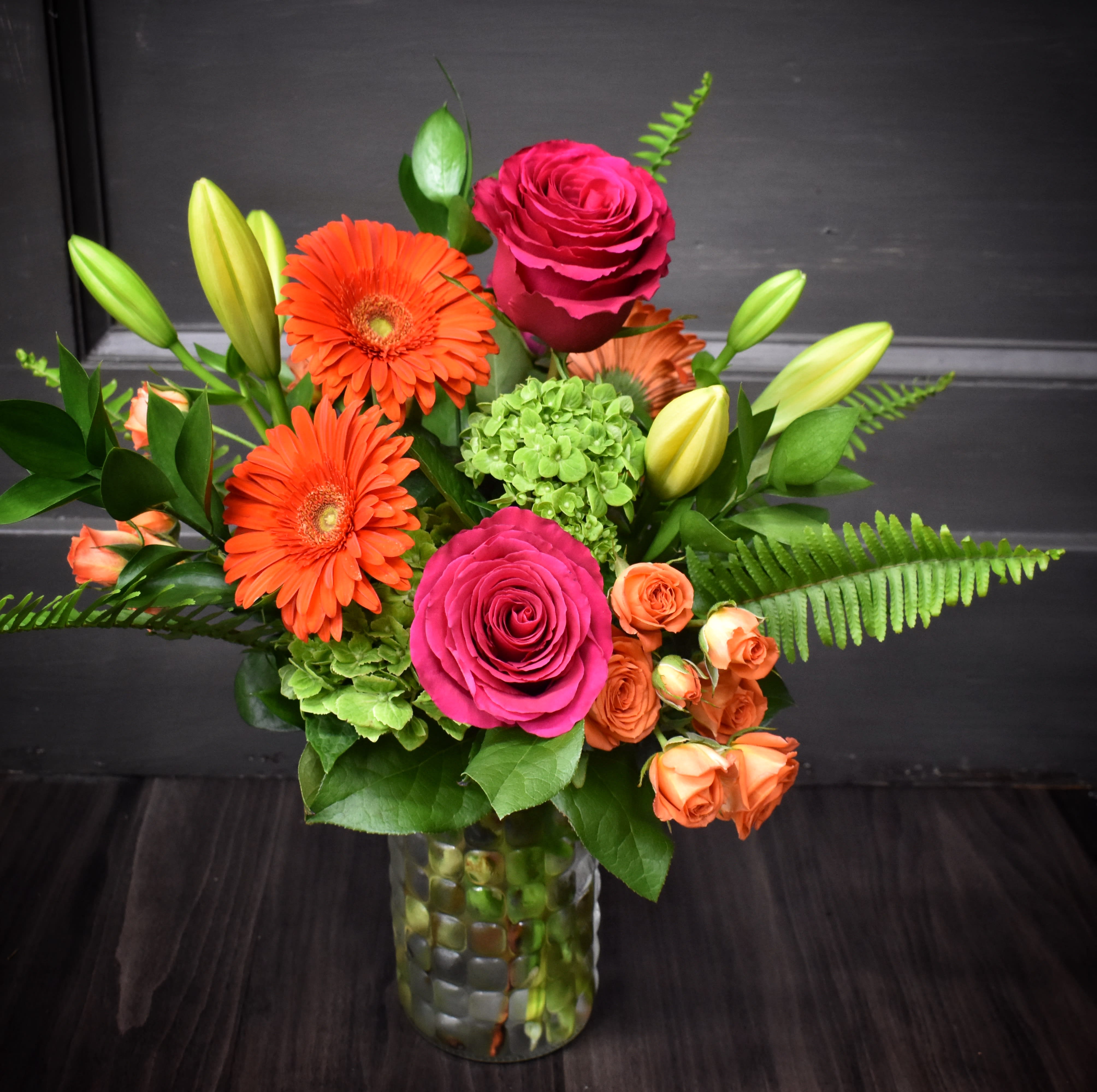 Bright mixed bouquet with pink roses, orange gerberas, and lilies in a glass vase