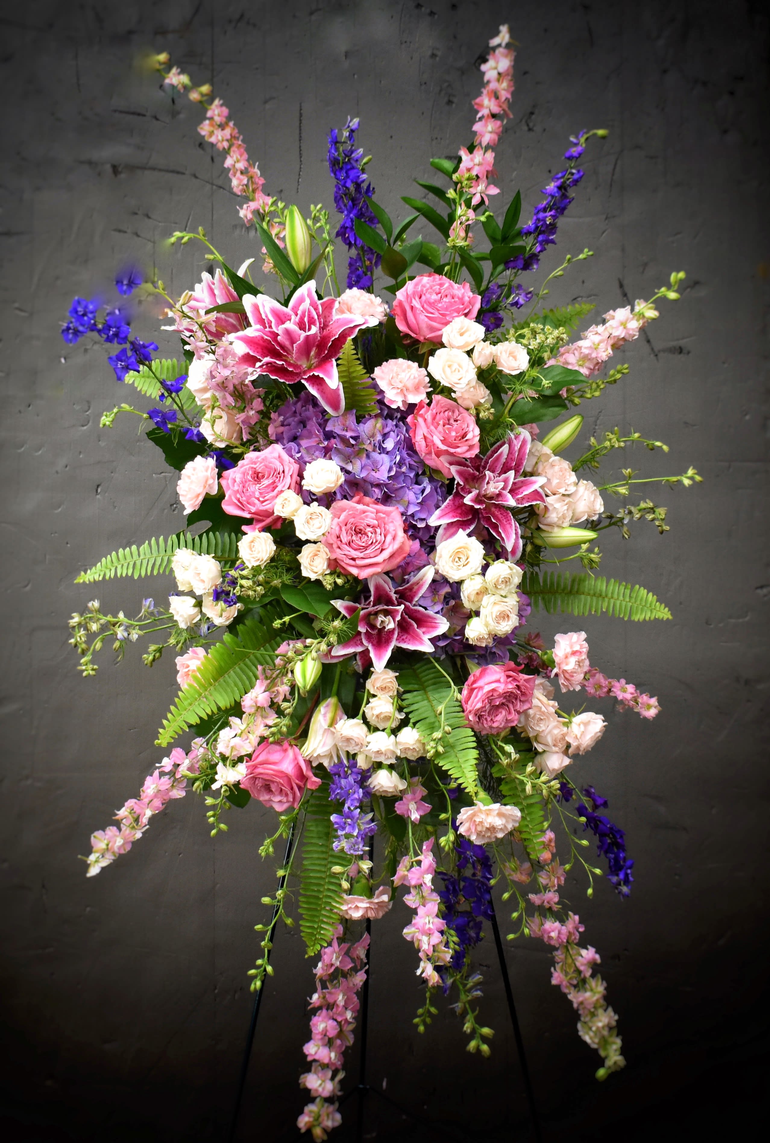Tall floral spray with pink roses, lilies, and purple blooms on a stand