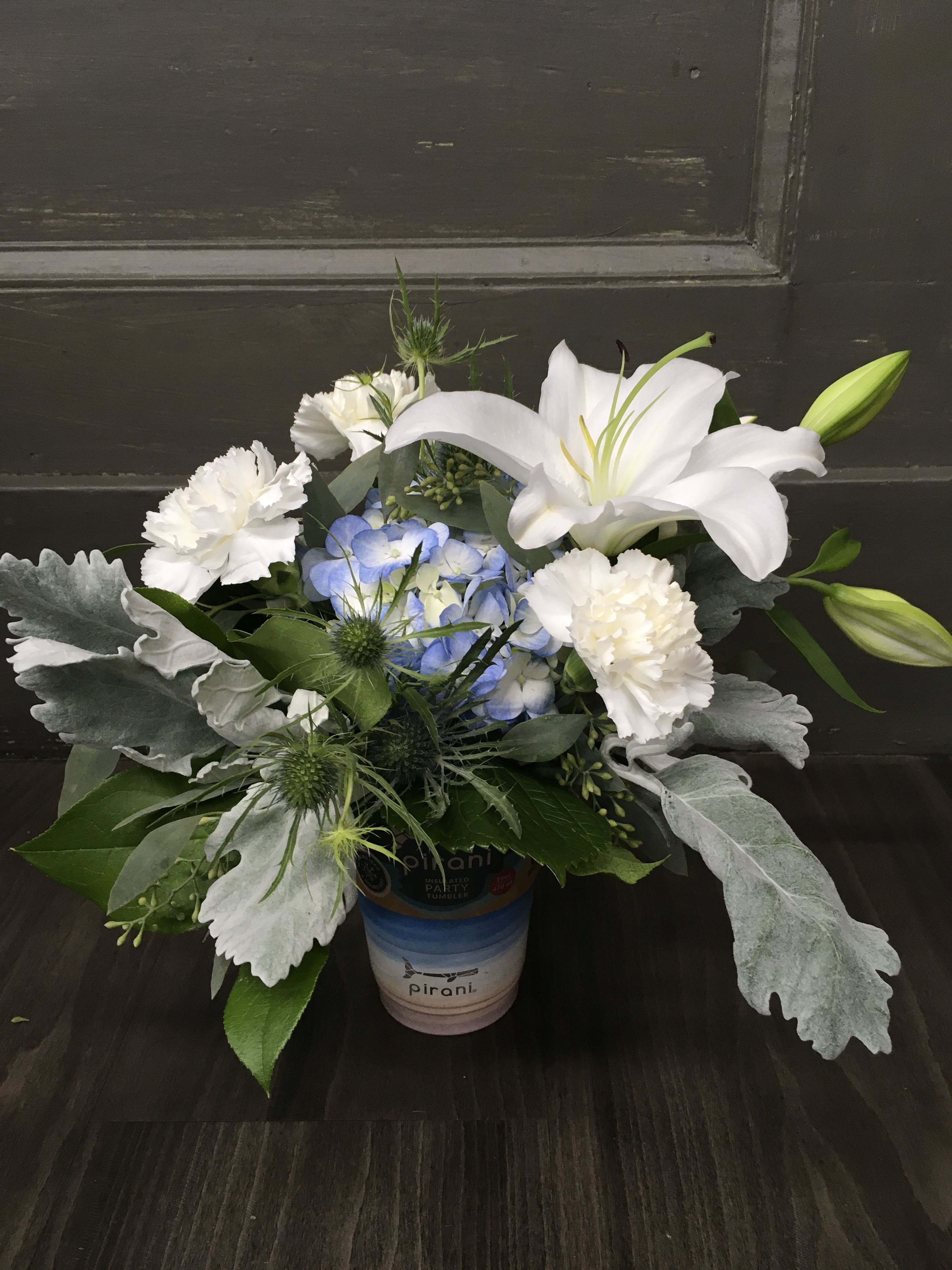 White lilies and carnations with blue hydrangea in a small container