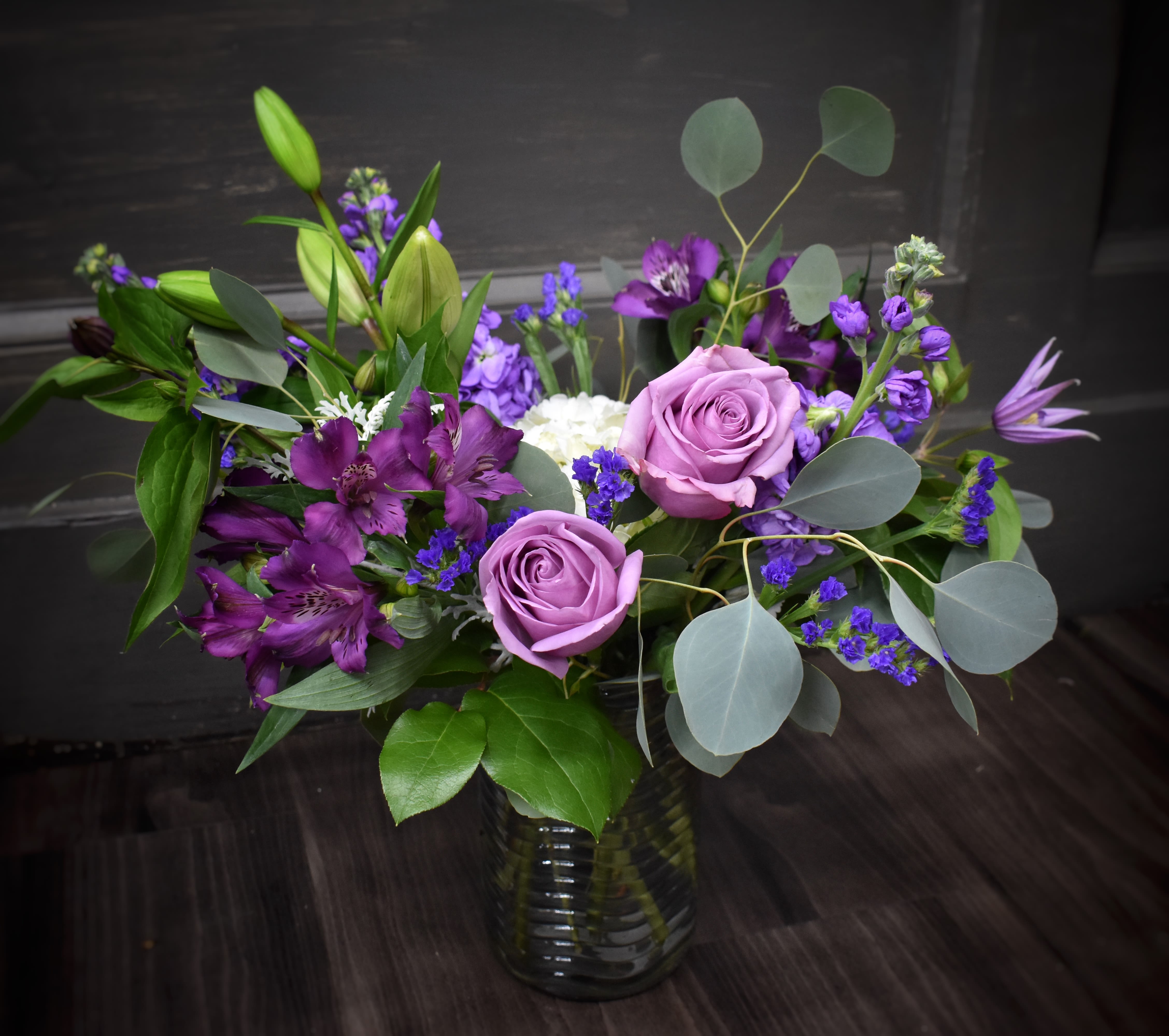 Purple roses and mixed purple flowers in a glass vase