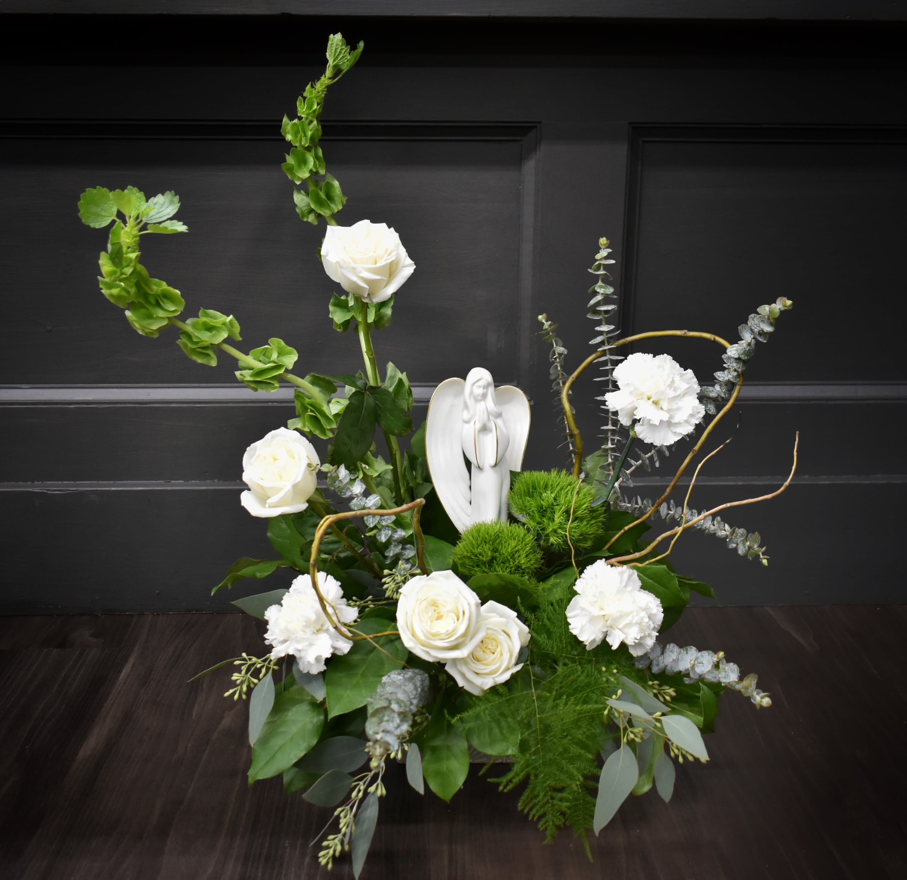 White roses and carnations arranged with greenery and a small angel figurine