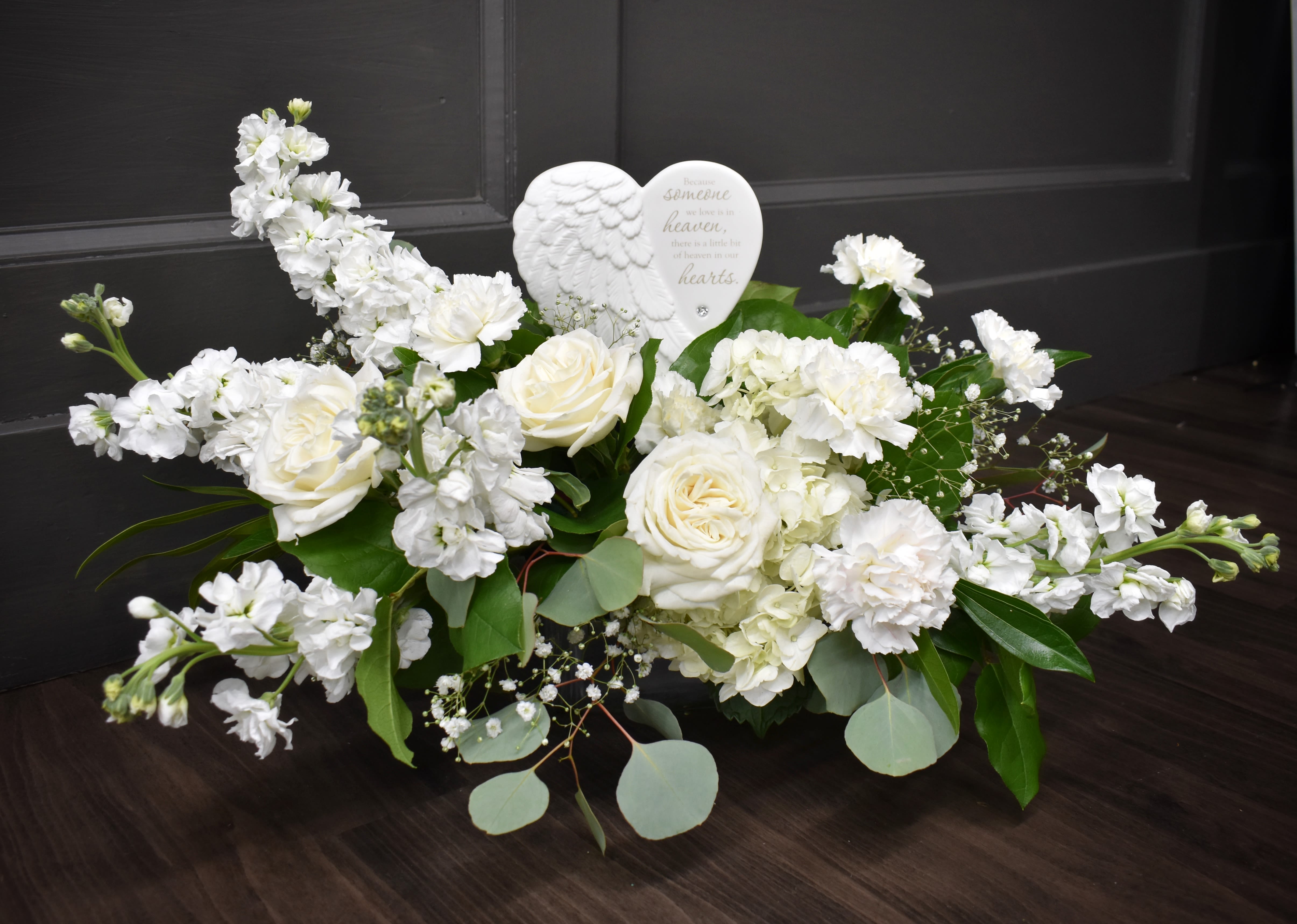 White floral arrangement with roses and carnations around a heart ornament