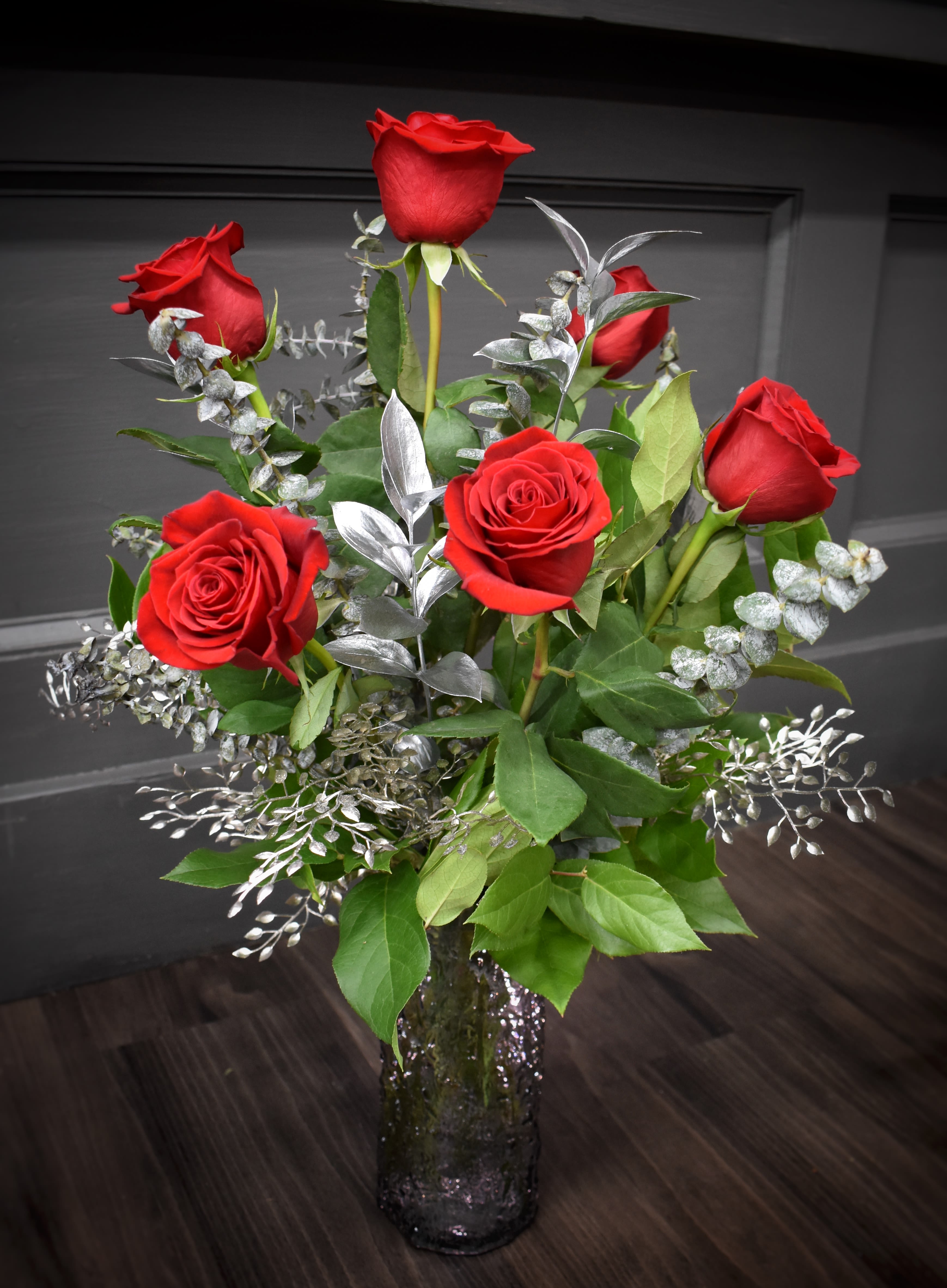 Red roses arranged in a clear glass vase with silver foliage