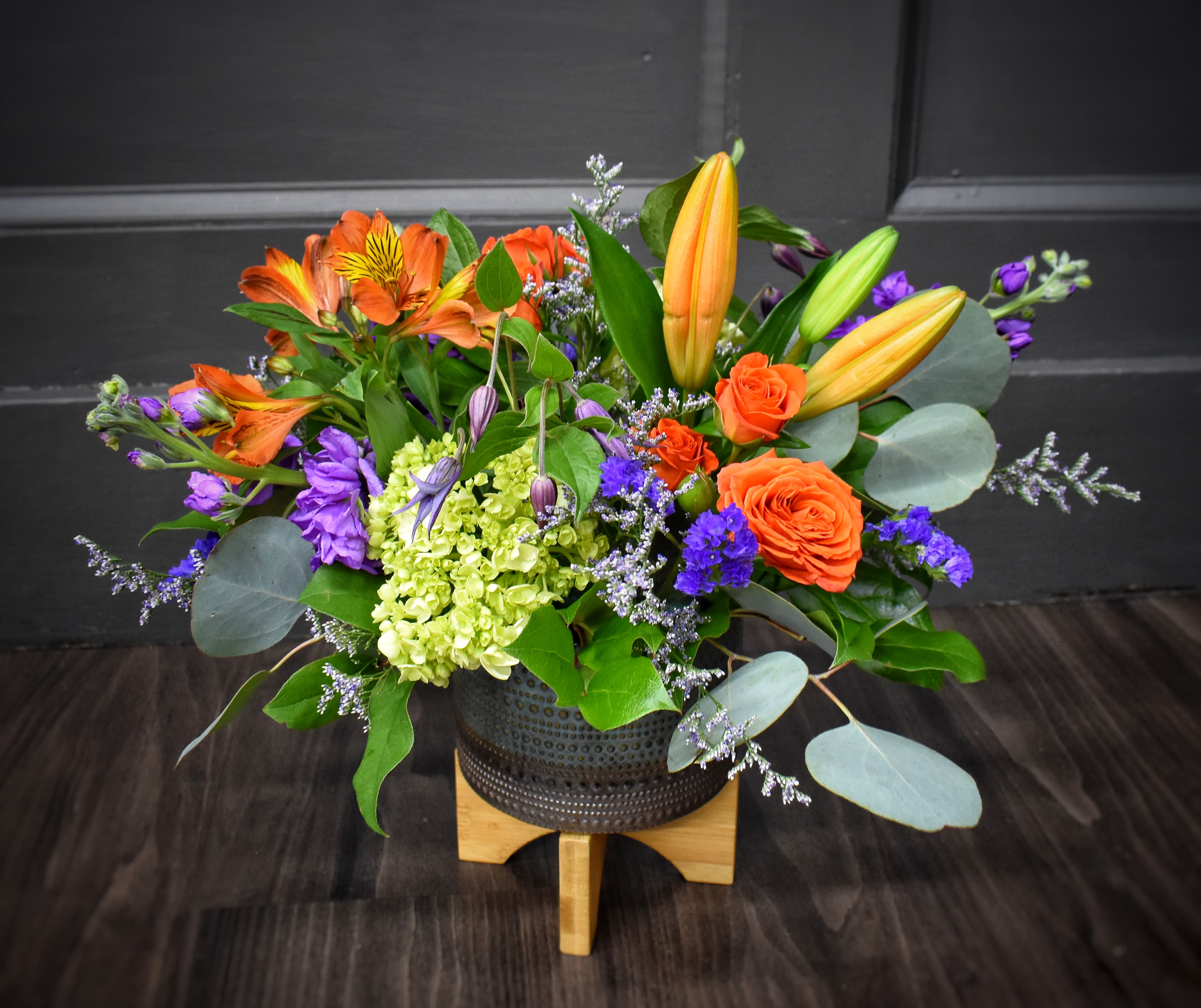 Color Burst - Available for local St Cloud, MN area delivery only - A brightly colored centerpiece designed with lilies, alstromeria, spray roses and more! This design comes delivered in a textured pottery container, nice for a keepsake. Approx. 12"h x 14"w