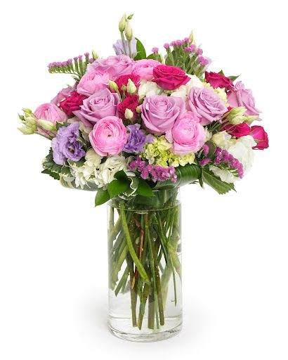Tall glass vase of pink and lavender roses with mixed pastel flowers in a rounded arrangement