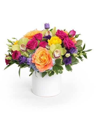 Low mixed arrangement of bright roses, orchids, and lisianthus in a white cylinder vase