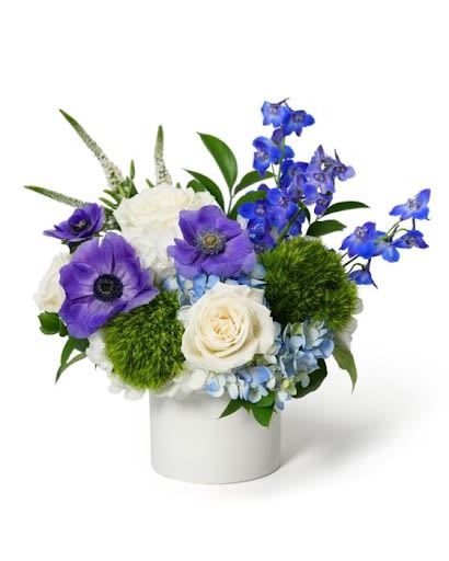 Compact blue and purple flower arrangement with white roses in a white ceramic cylinder vase