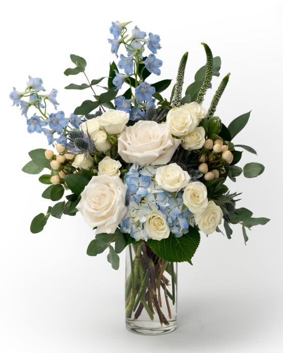 White roses and blue hydrangea with blue delphinium in a clear glass vase