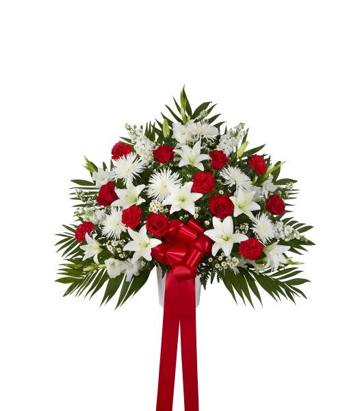 Fan-shaped standing arrangement of red roses and carnations with white lilies and mums, finished with a red bow and ribbon