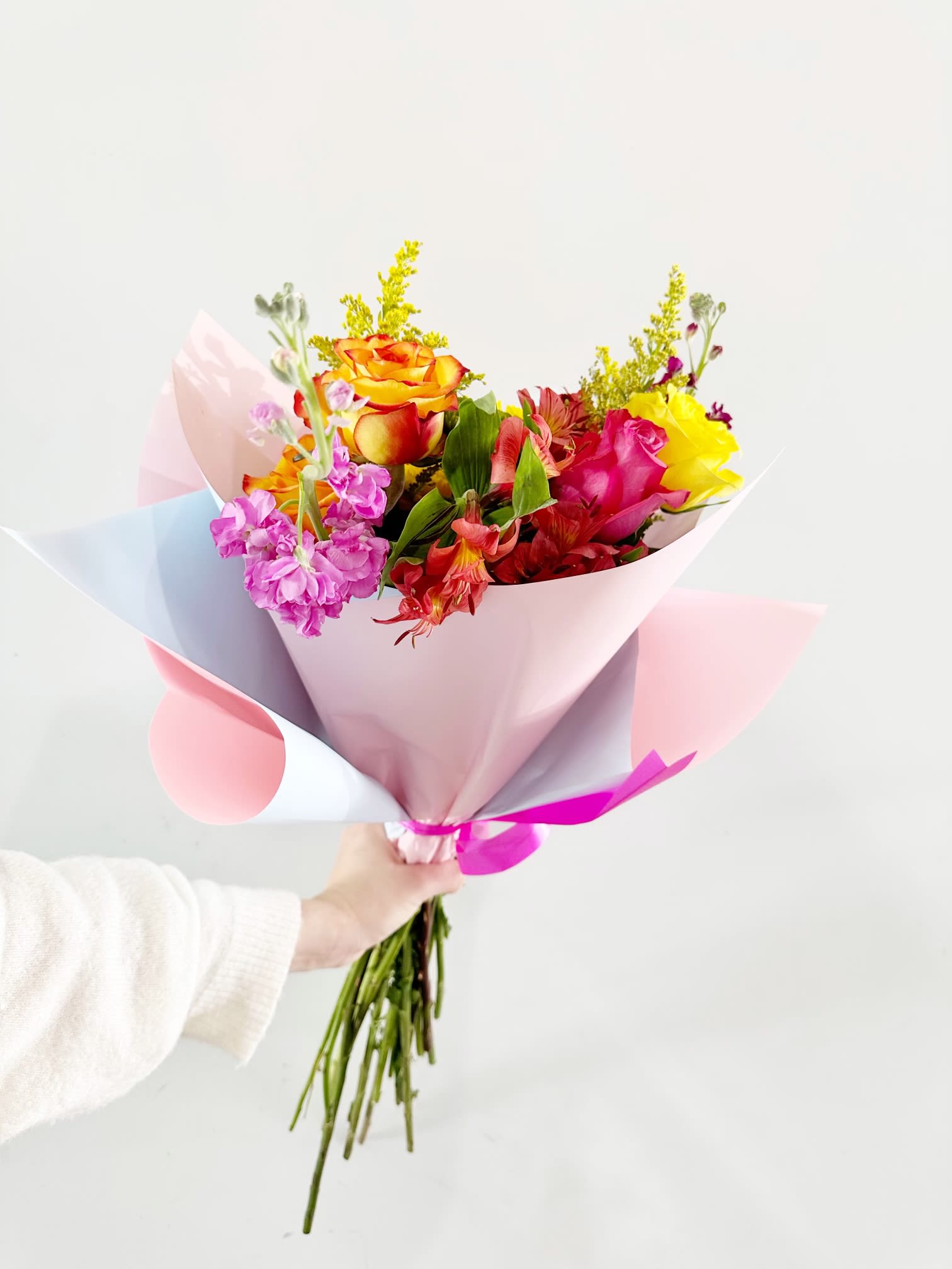 Handheld bouquet of multicolored roses and mixed blooms in pastel wrap