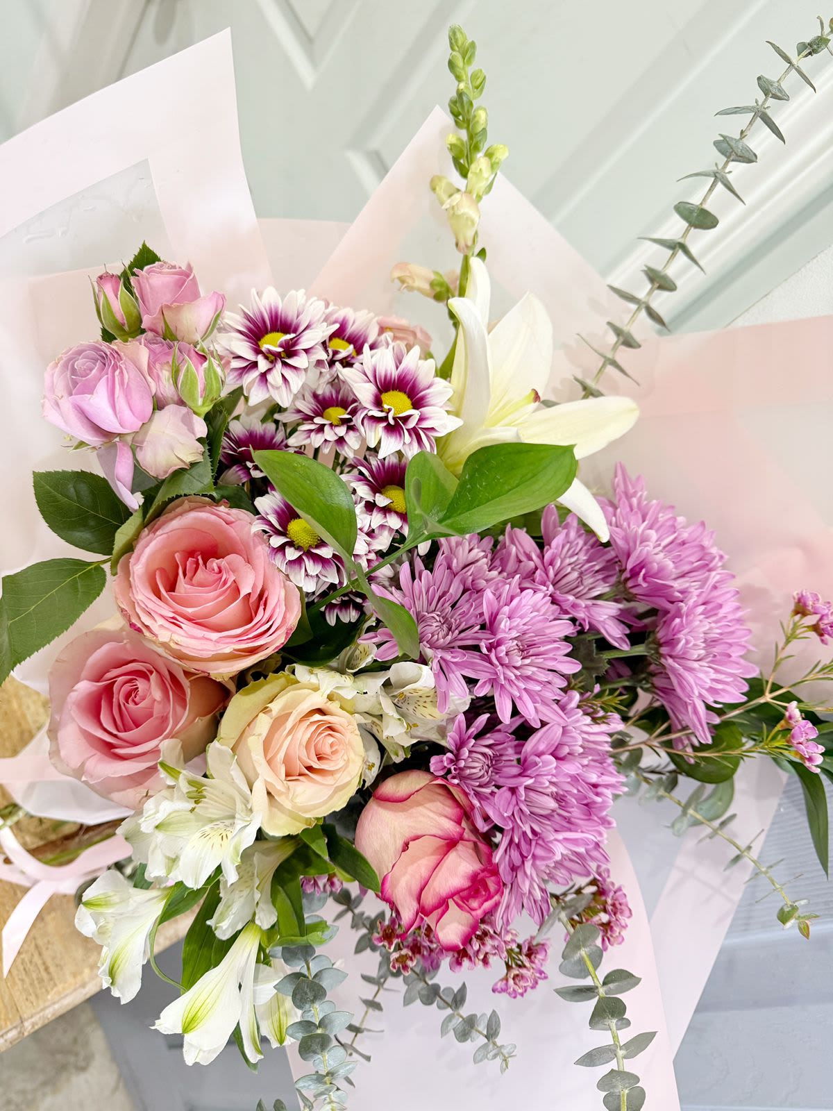 Bouquet of pink roses, purple daisies, and white lilies in pale wrapping