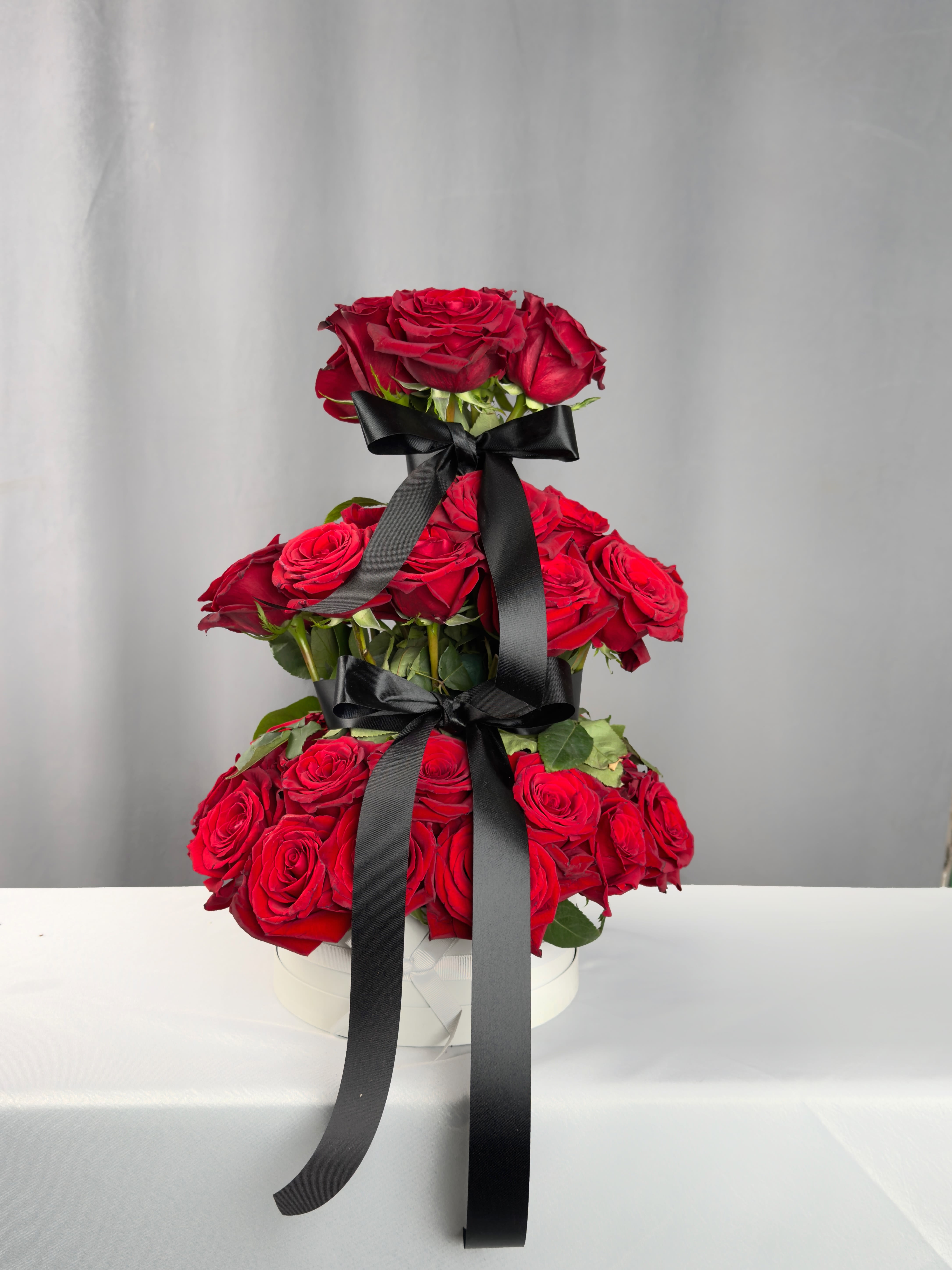Tiered arrangement of red roses with black ribbon in a white box
