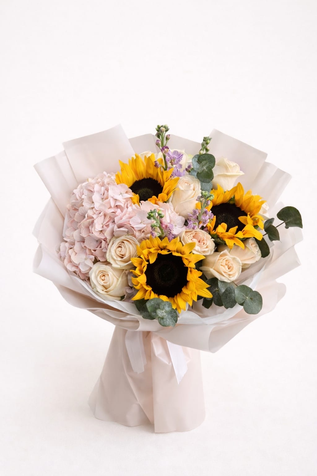 Bouquet of sunflowers, pale roses, and pink hydrangea wrapped in white paper