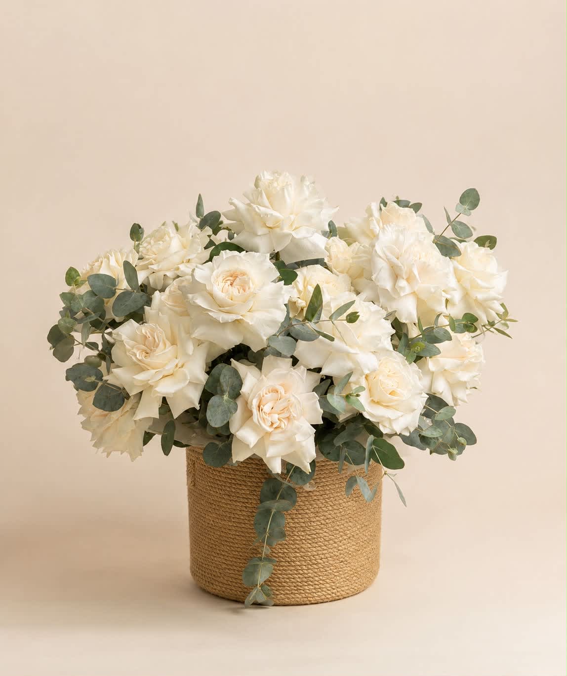 White roses arranged in a woven basket with eucalyptus