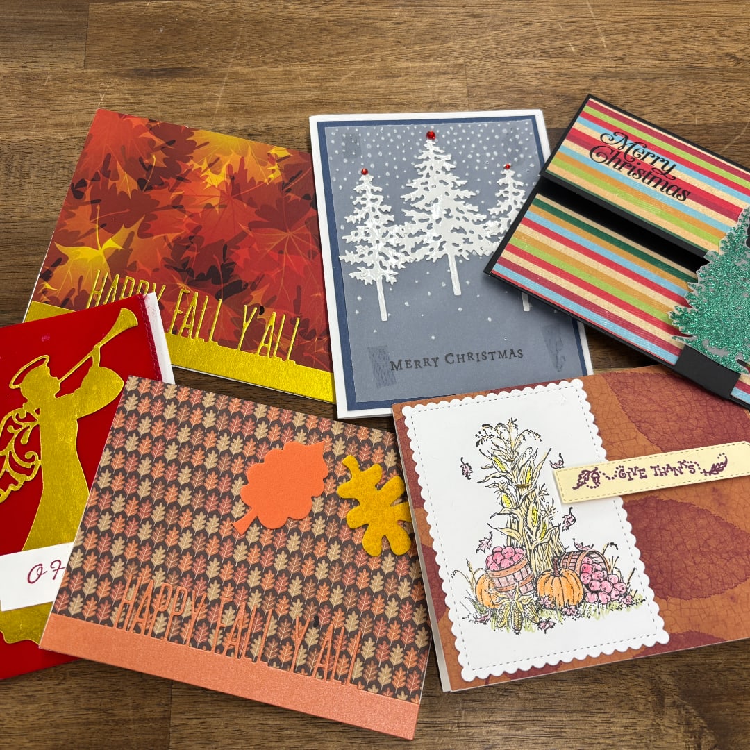 Assorted handmade greeting cards with fall and Christmas designs on a wooden surface