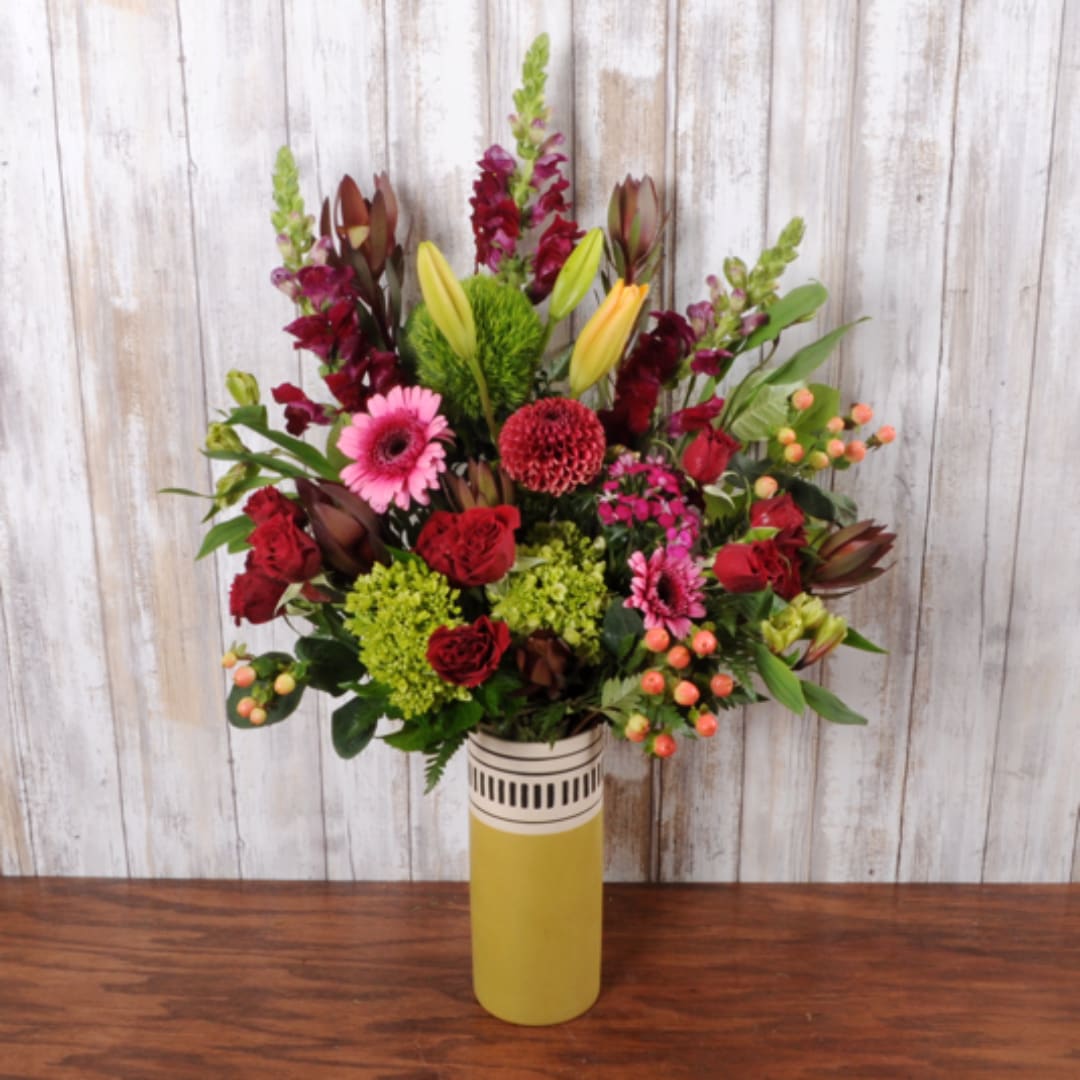 Tall mixed bouquet in a yellow vase with red, pink, and green blooms