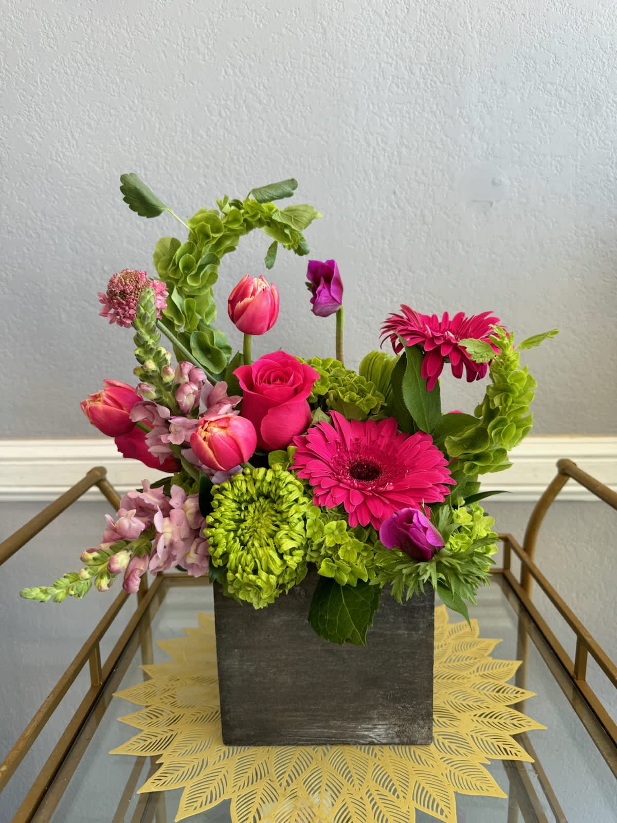 Bright pink and green mixed flower arrangement in a square dark vase