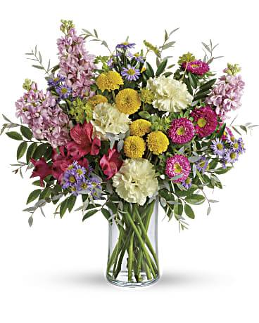 Mixed bouquet of pink, yellow, purple, and white flowers in a glass vase