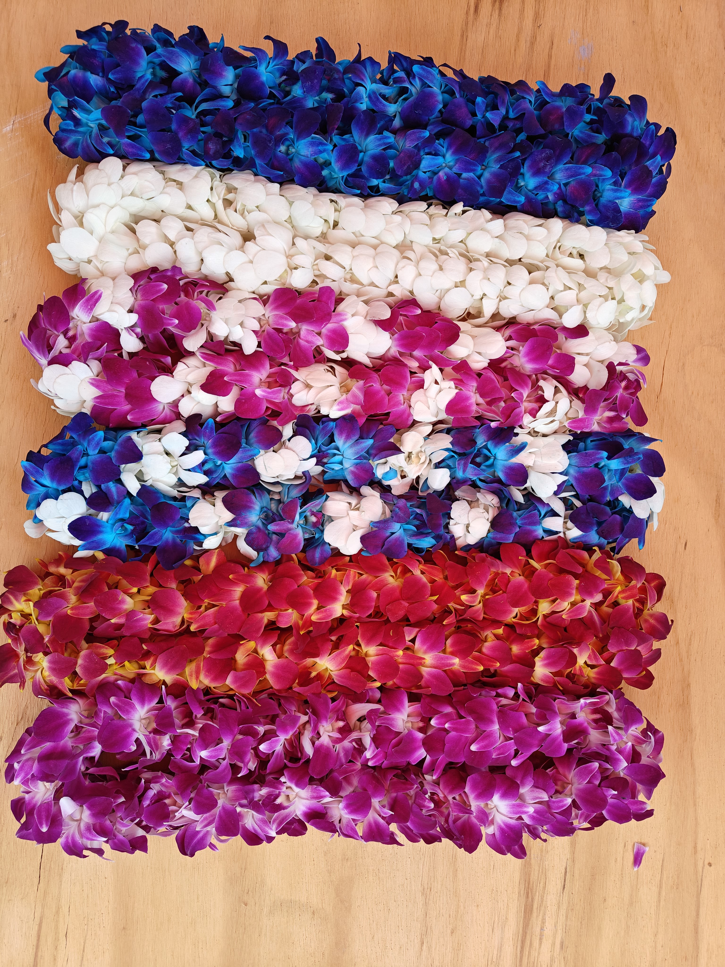 Stacked orchid leis in blue, white, pink, and red on a wooden surface