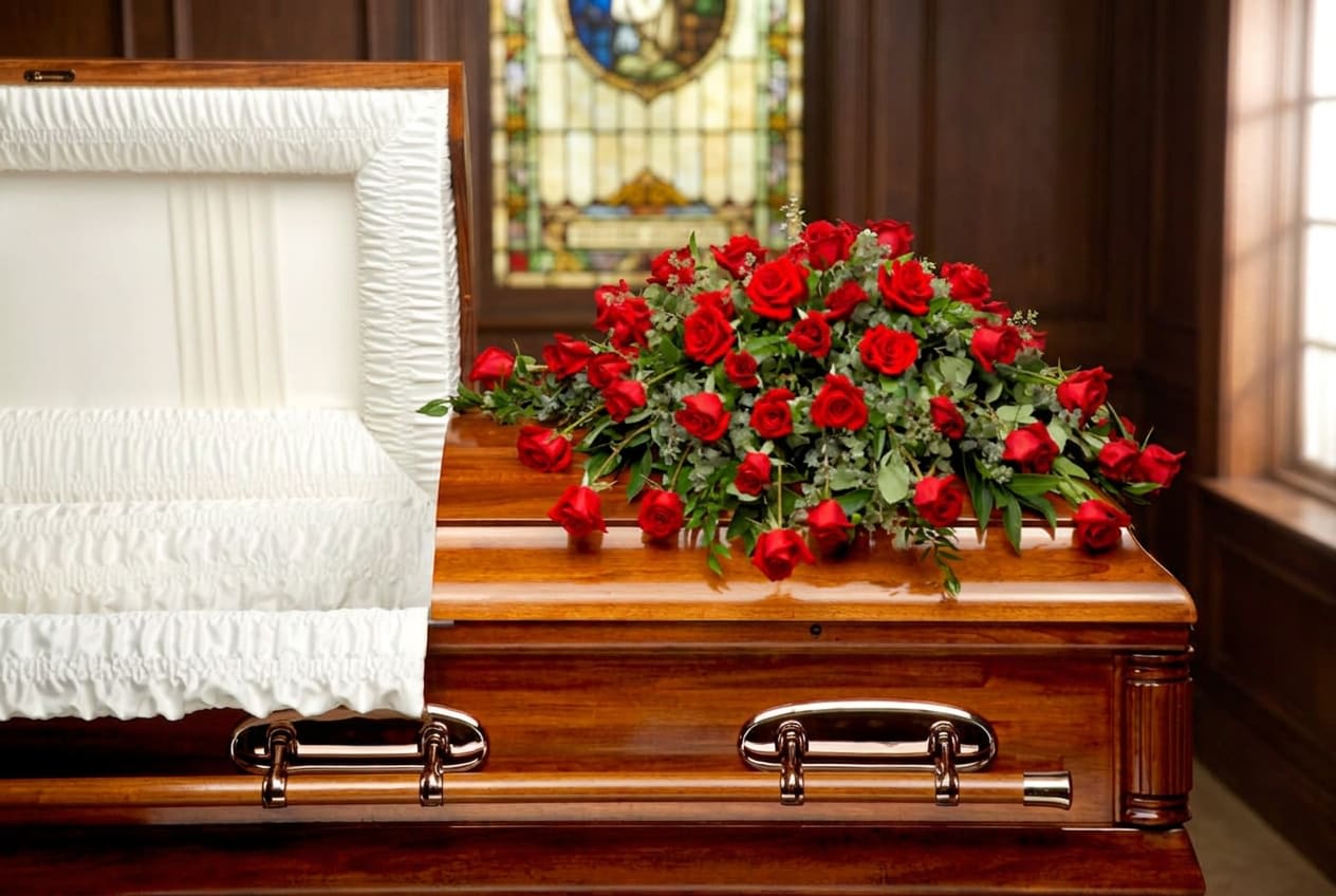 Red rose spray on a wooden casket with a white interior lining