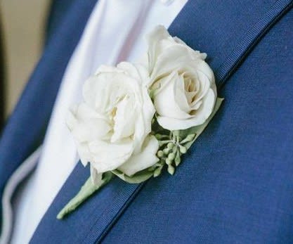 White rose boutonniere pinned to a blue suit jacket
