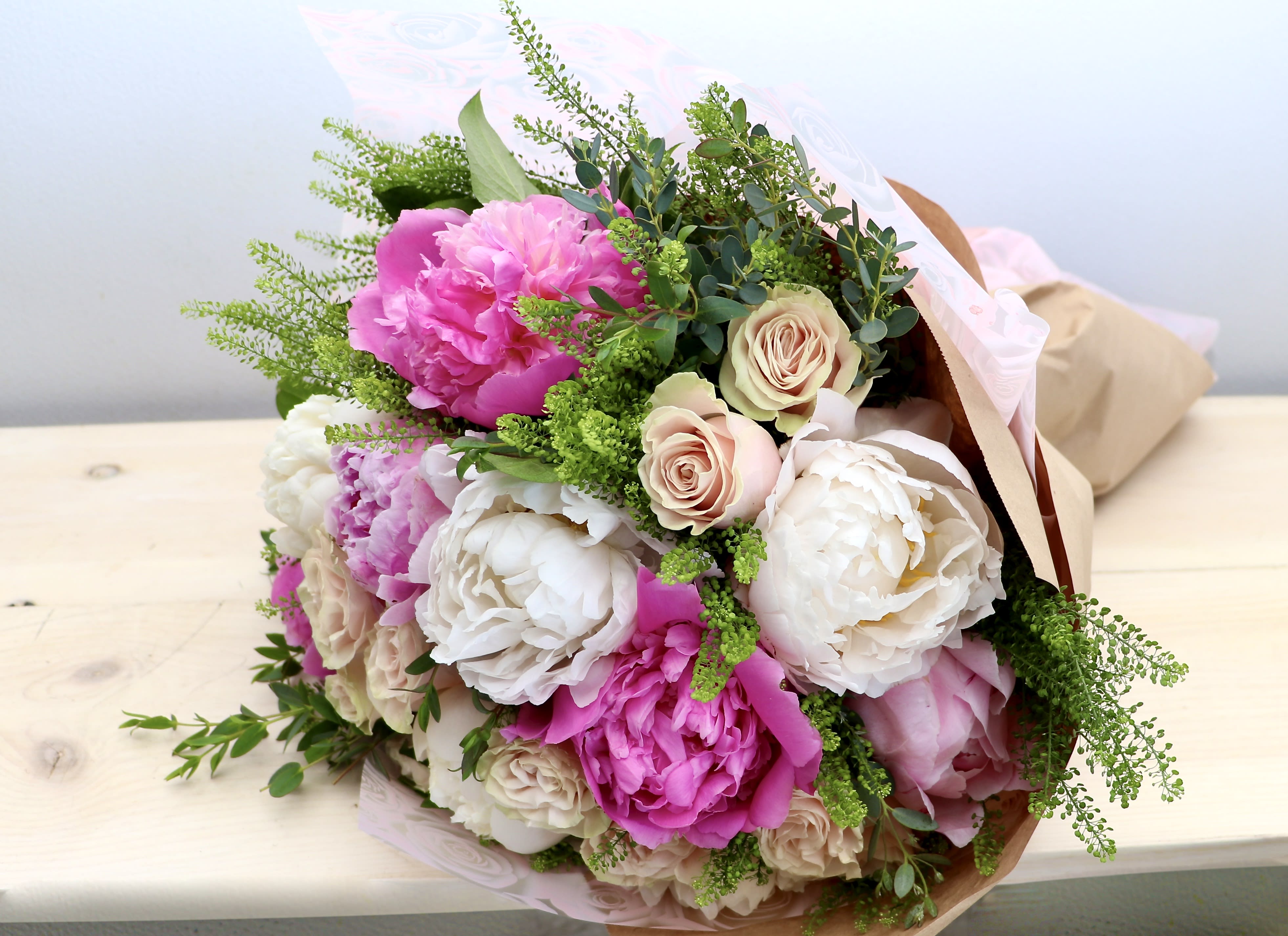 Hand-tied bouquet of pink peonies and cream roses wrapped in kraft paper