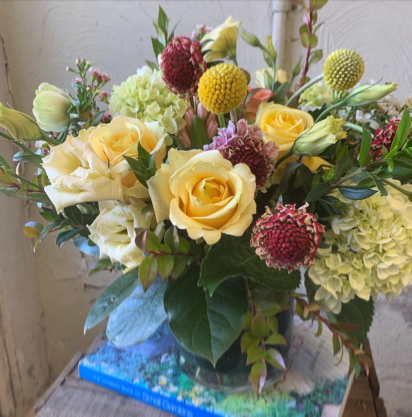 Yellow roses and pale hydrangeas in a glass vase with round accent blooms