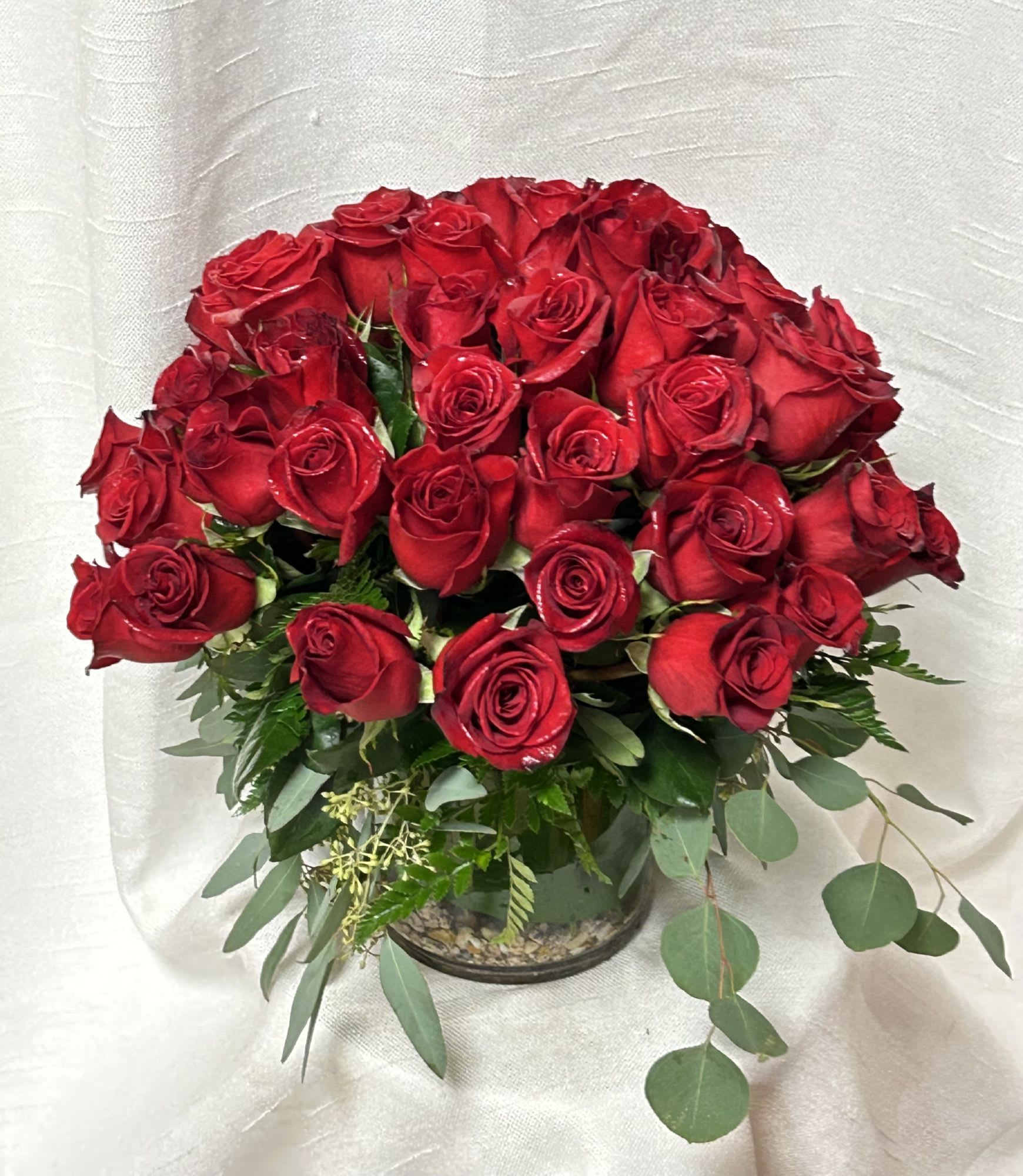 Bouquet of red roses in a glass vase with mixed greenery