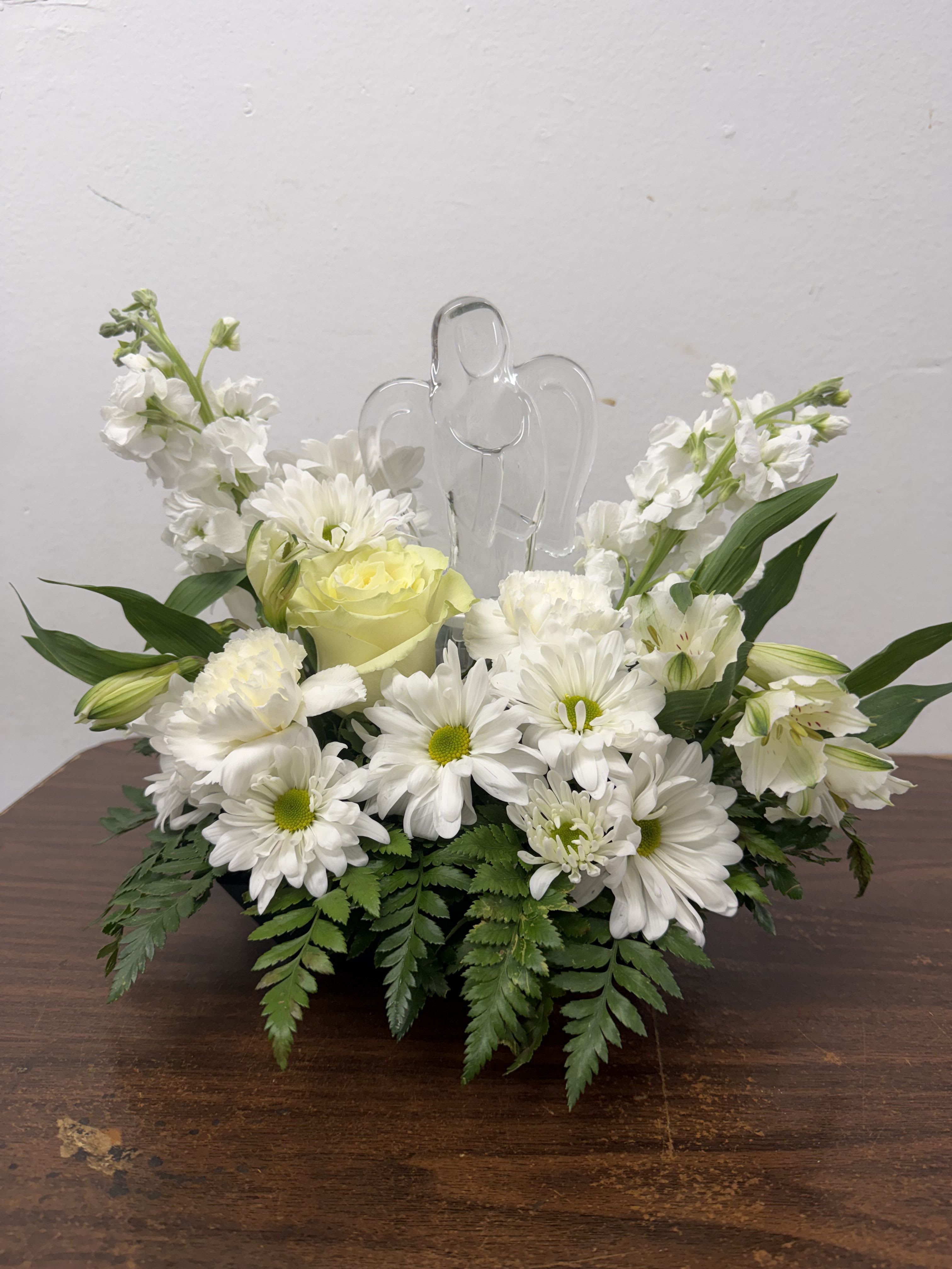 White floral arrangement with daisies and roses around a clear angel figurine
