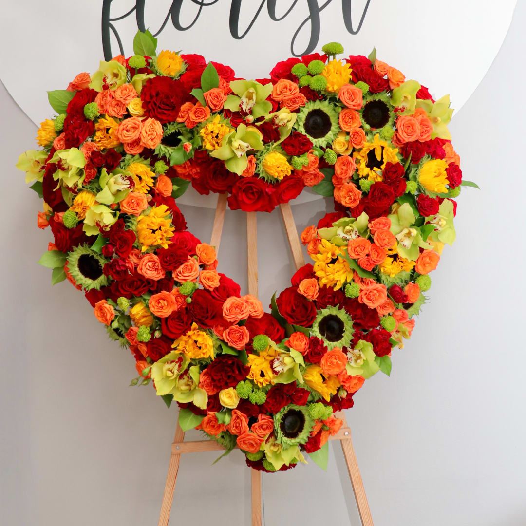 Heart-shaped floral arrangement on an easel with red, orange, yellow, and green blooms