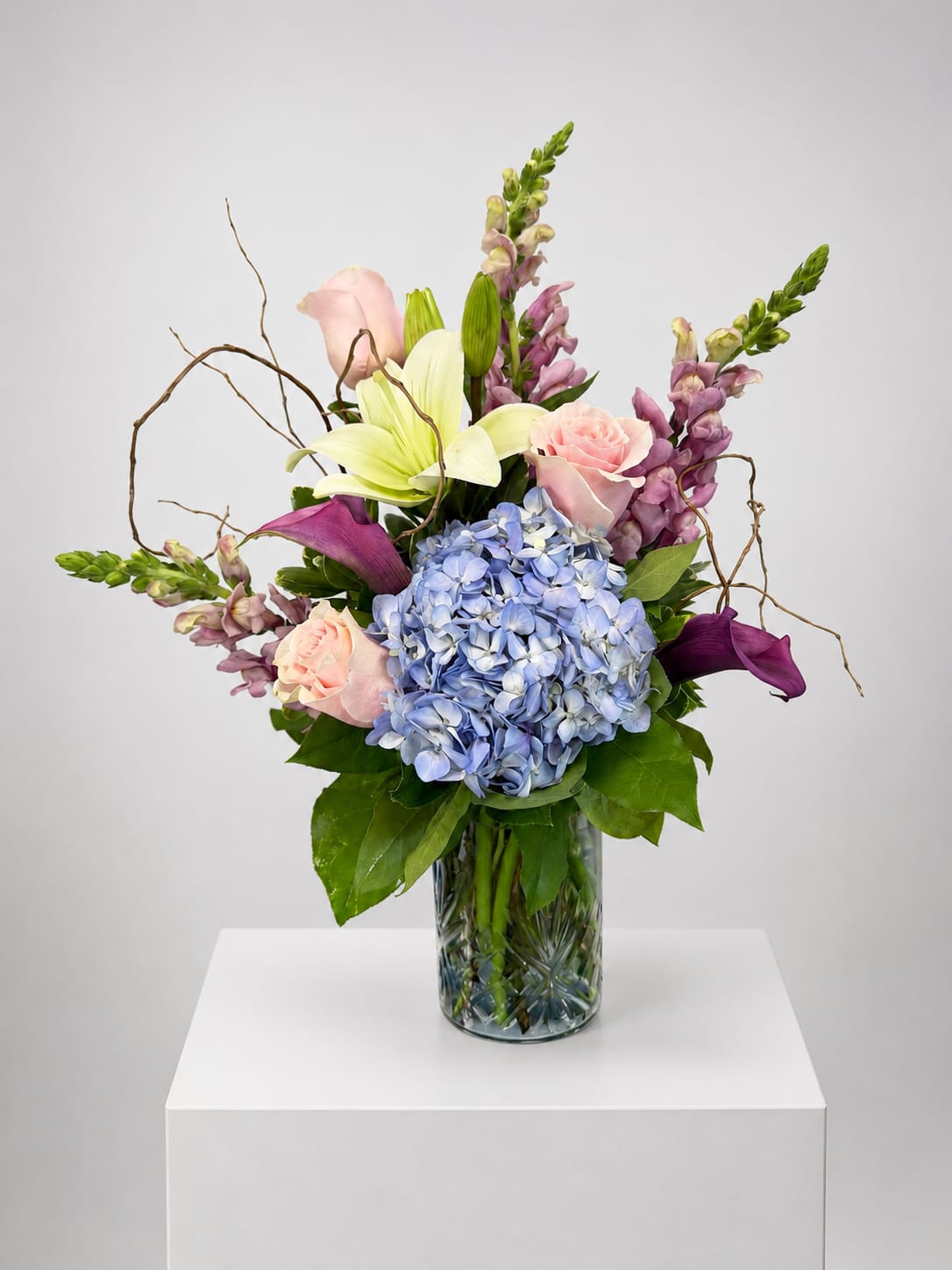 Mixed bouquet in a glass vase with blue hydrangea, pink roses, lilies, and purple blooms