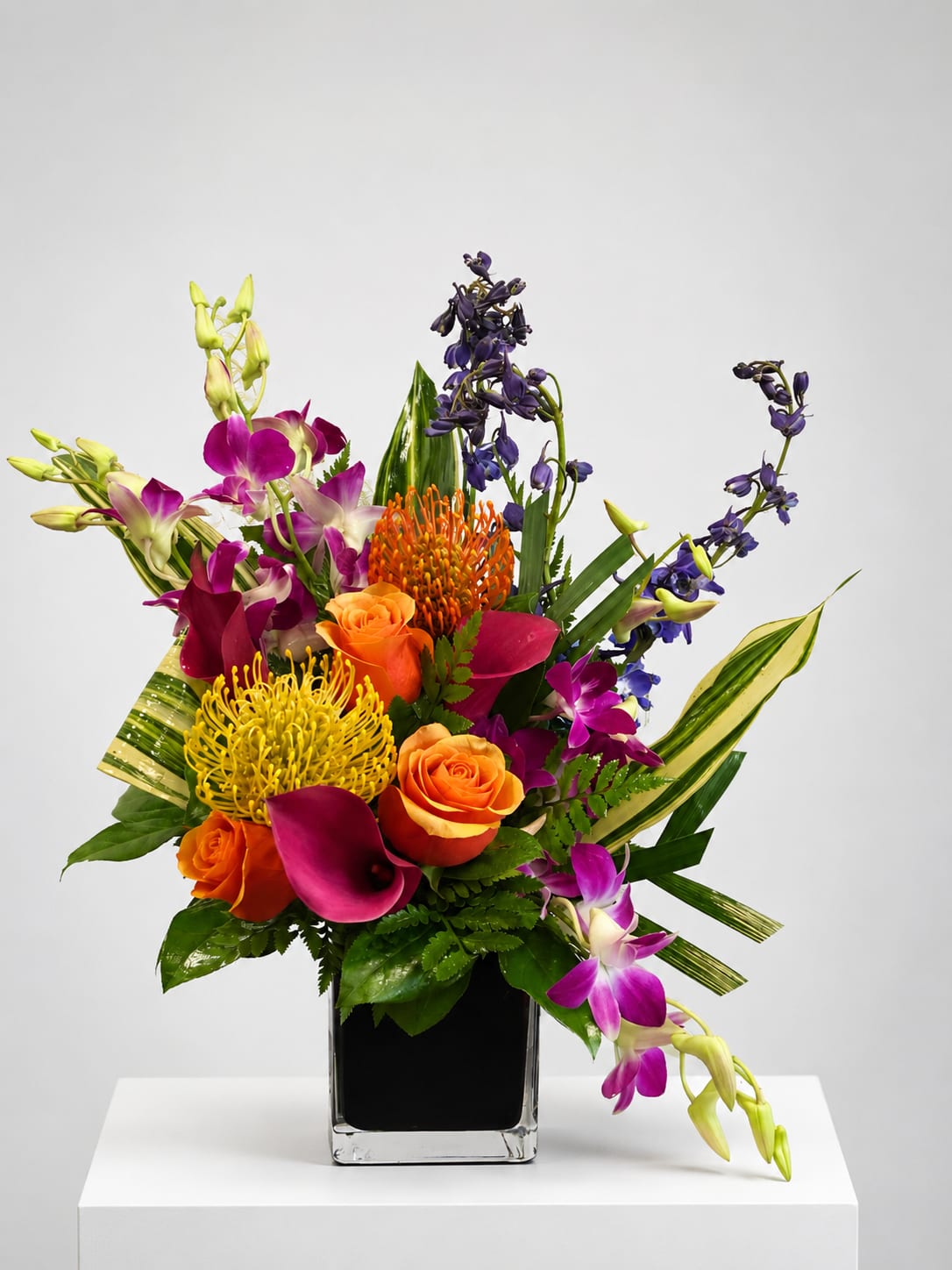 Colorful tropical bouquet in a square glass vase with orange roses and purple orchids
