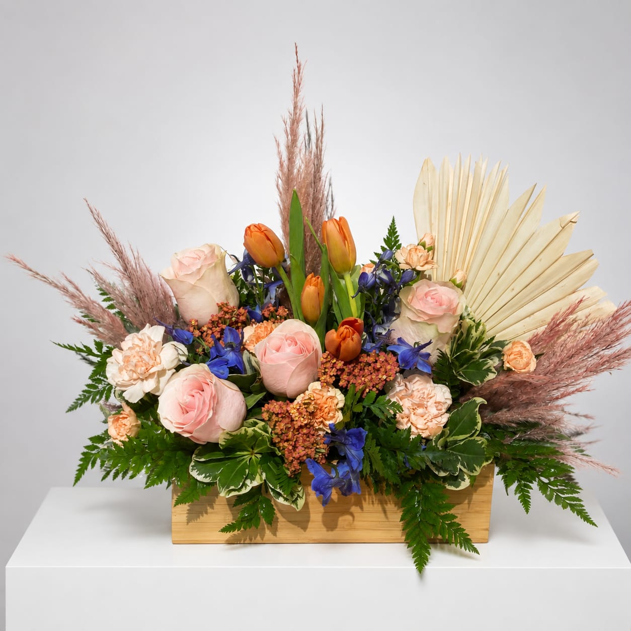 Mixed bouquet with pink roses, orange tulips, and blue flowers in a wooden box
