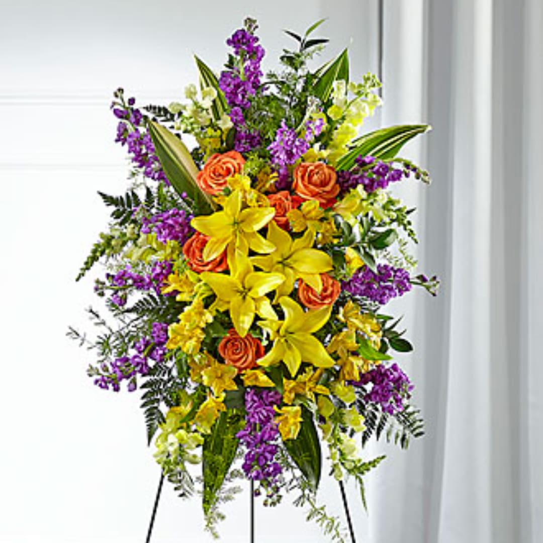 Tall floral spray with yellow lilies, orange roses, and purple flowers on a stand
