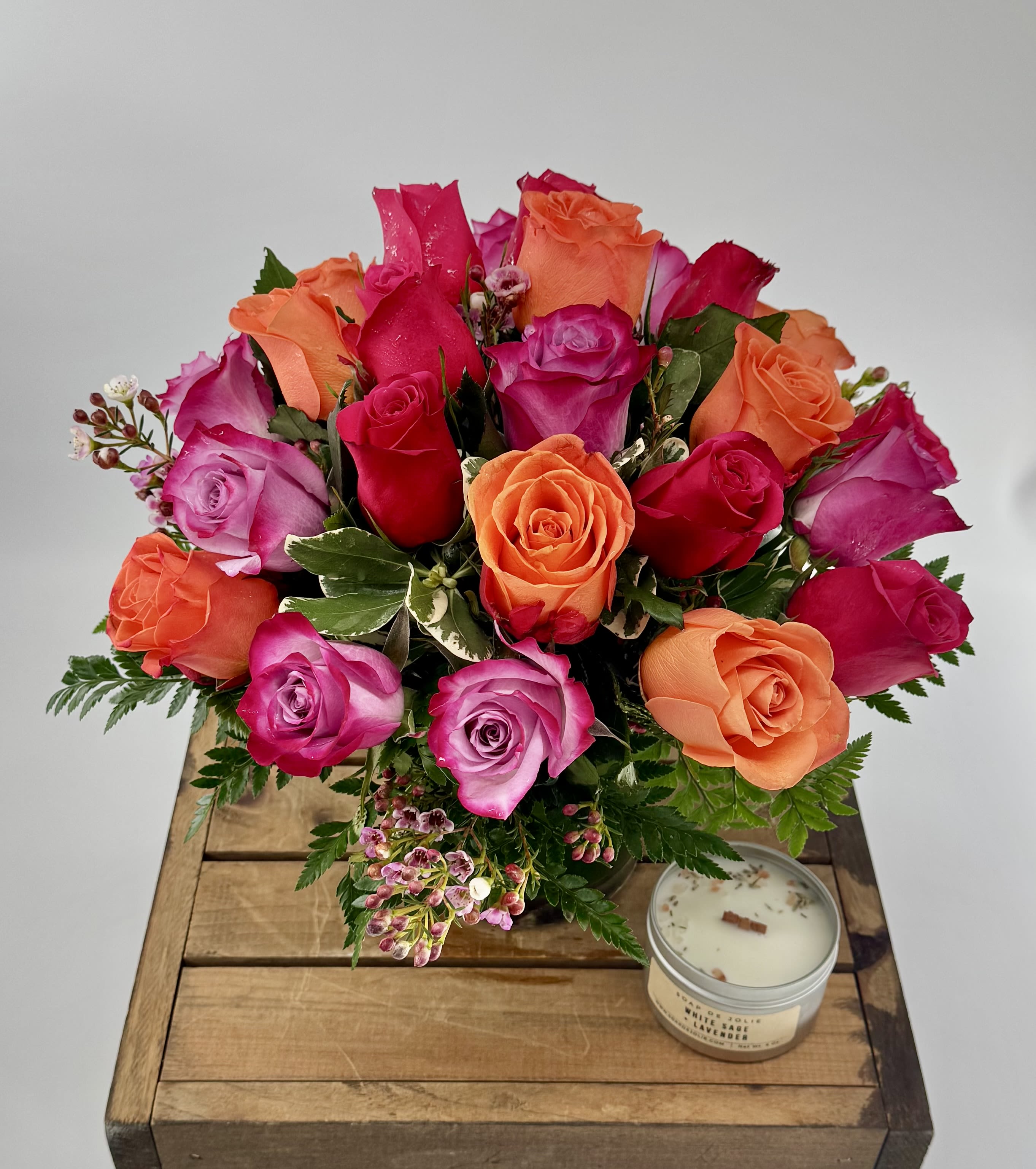 Bouquet of pink, red, and orange roses with a candle on a wooden box