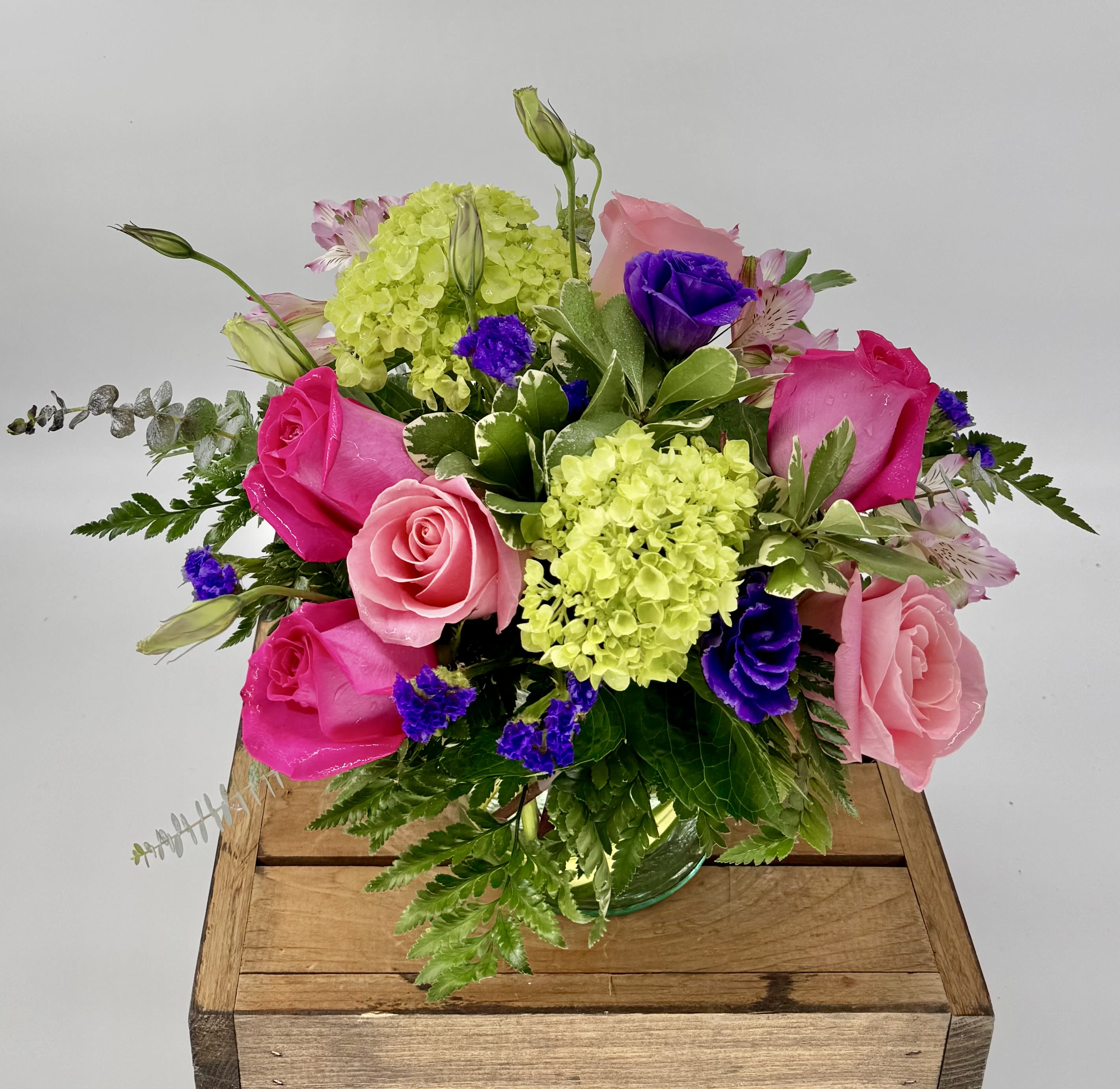 Spring Fling  - Elevate your special moments with this vibrant bouquet of hot and soft pink roses, lush green hydrangea, delicate Lisianthus, and purple statice—artfully arranged in a sleek 5x5" cylinder vase. 